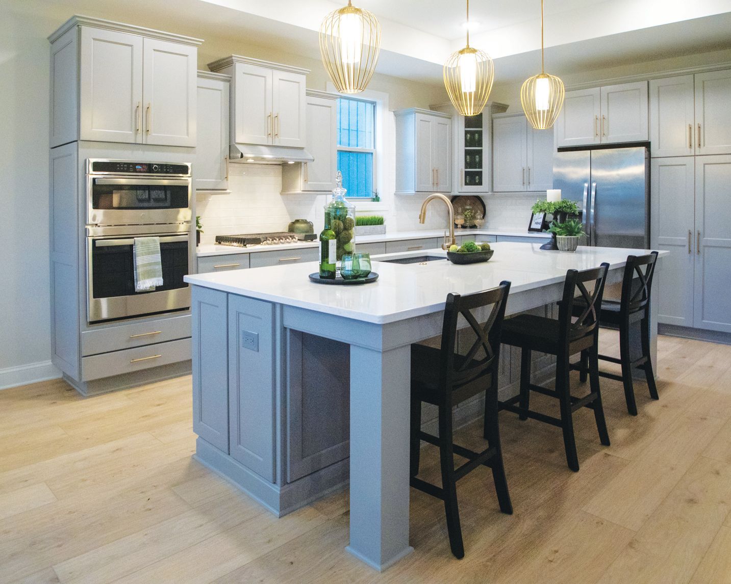 A modern kitchen featuring light blue cabinetry, stainless steel appliances, a white island with black stools, and wood floors.
