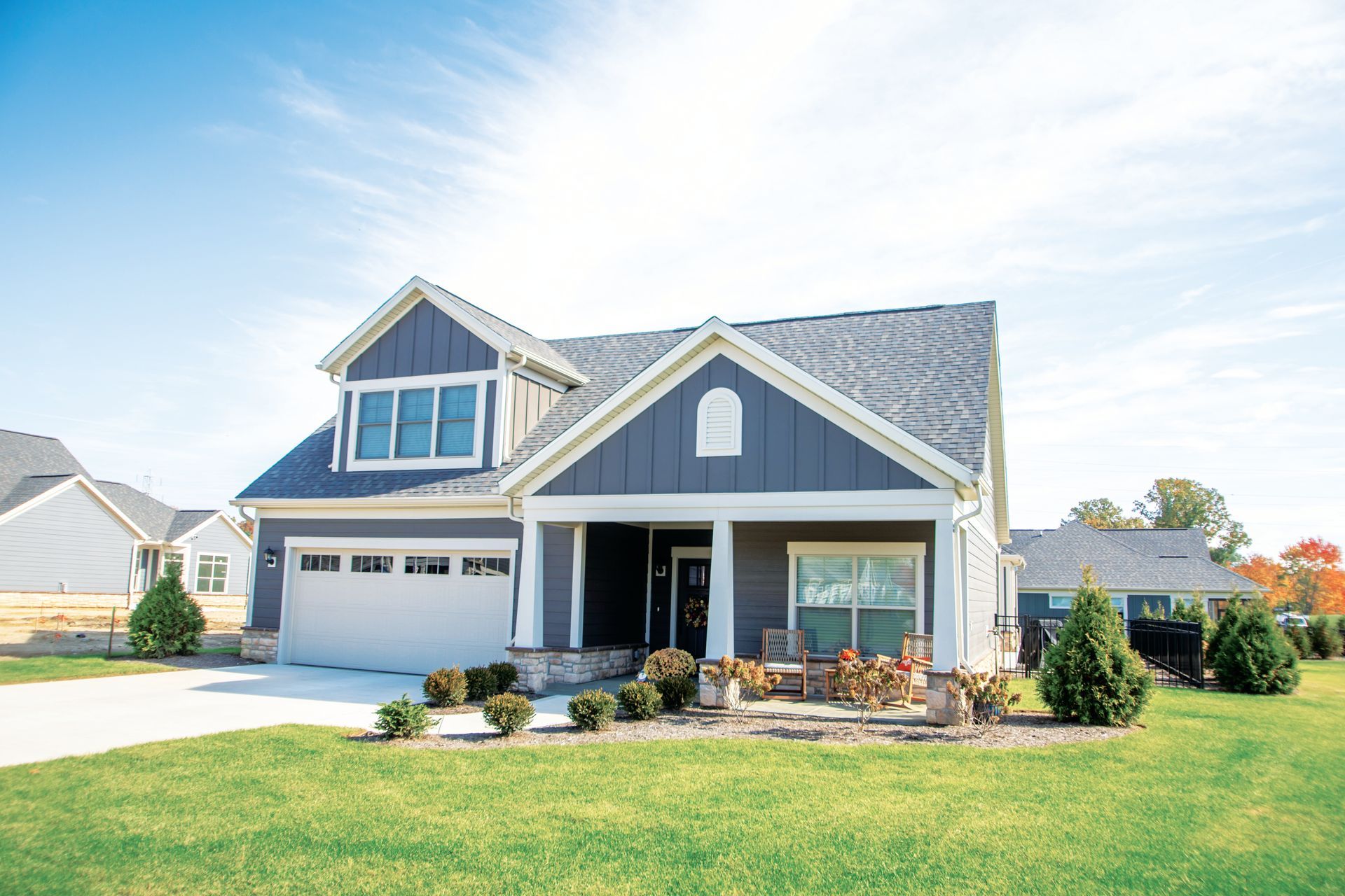 A single-story gray house with a two-car garage, white trim, and a gabled front porch under a clear blue sky.