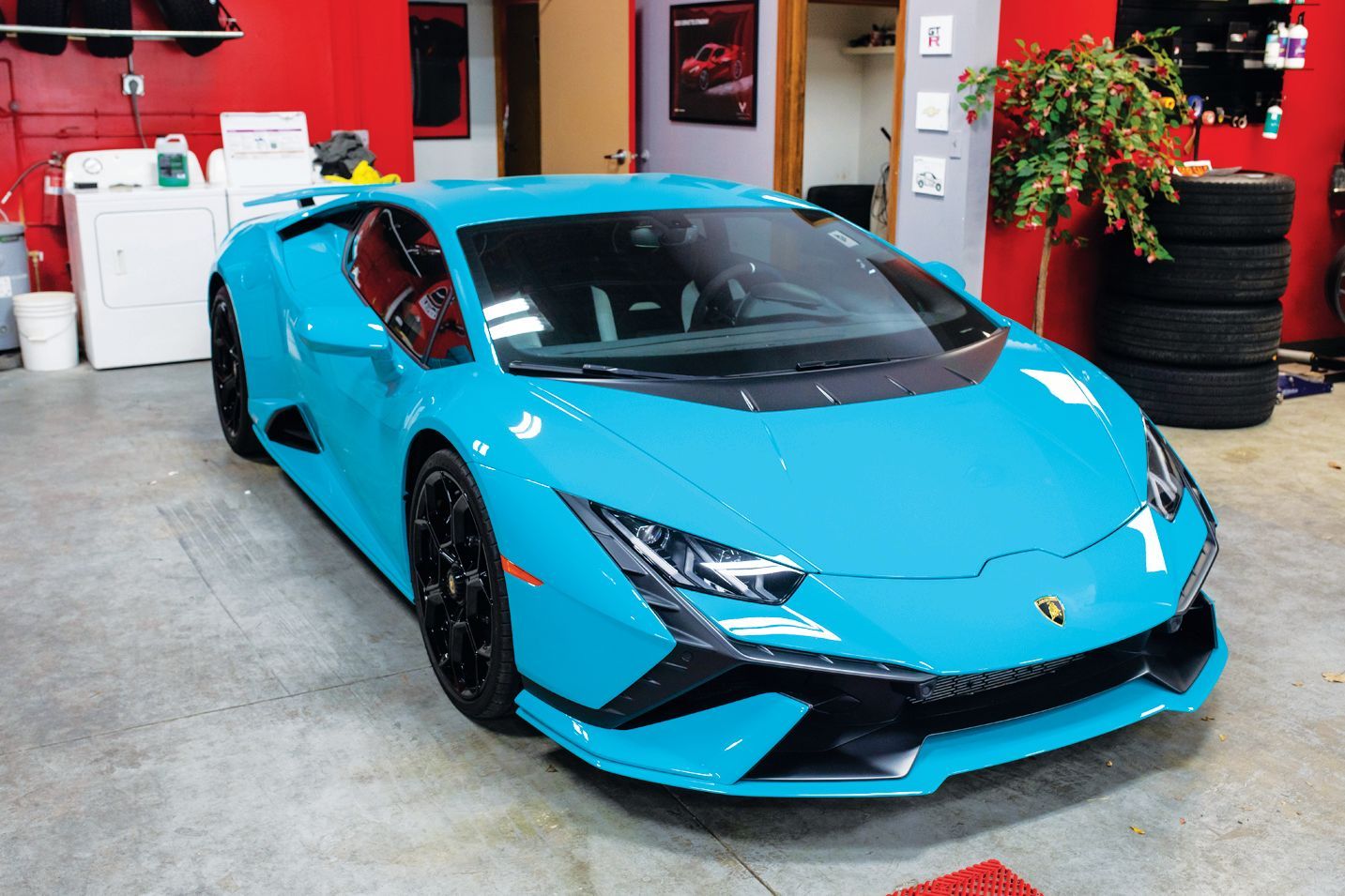 A bright blue Lamborghini sports car parked inside a garage next to a stack of tires.