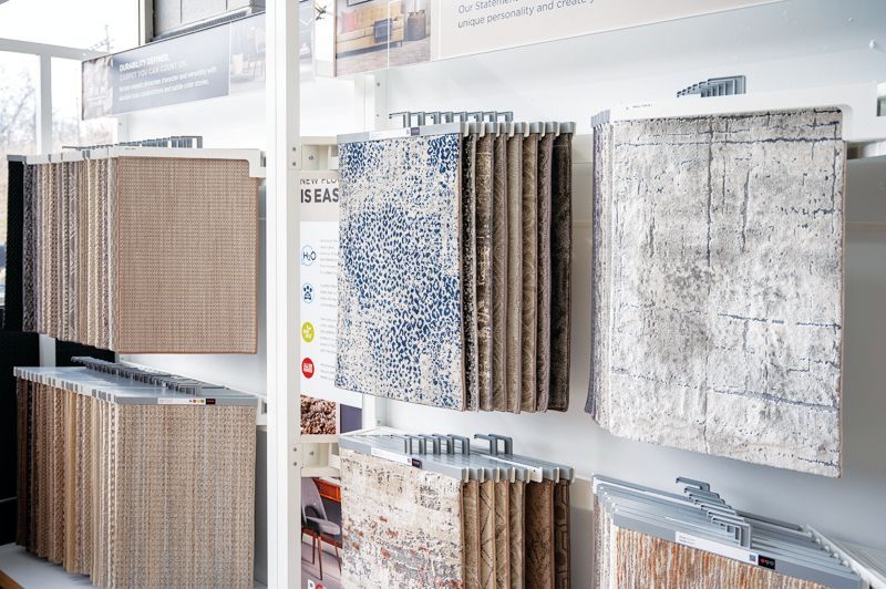 A store display featuring rows of hanging rug and carpet samples in various patterns, textures, and neutral color tones.