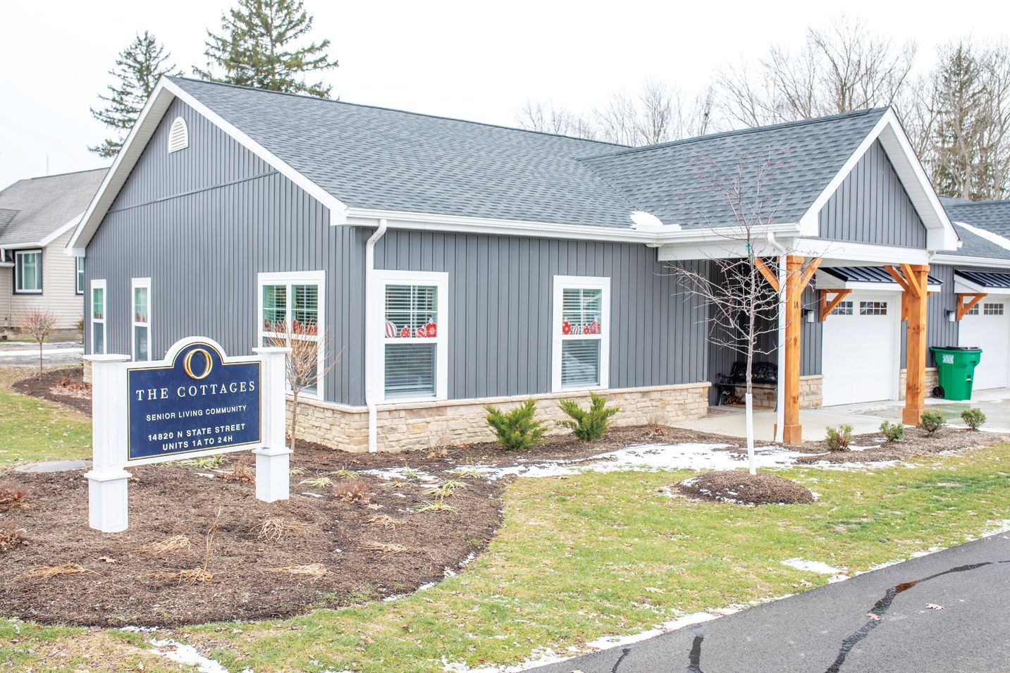 A modern, single-story building with dark gray vertical siding, stone accents, and wood supports in front of a garage.
