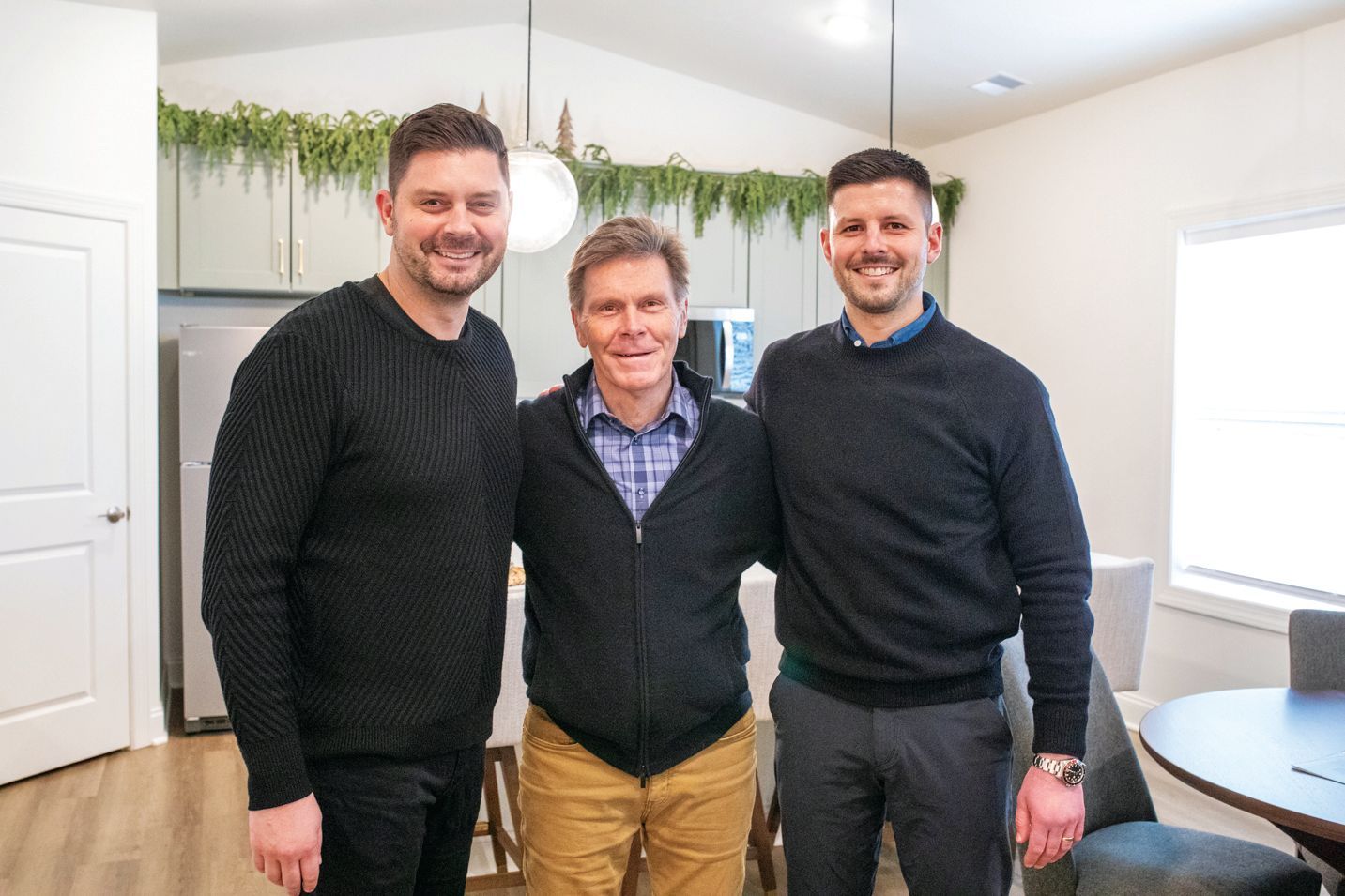 Three men standing side-by-side in a kitchen, smiling and posing for a photo.