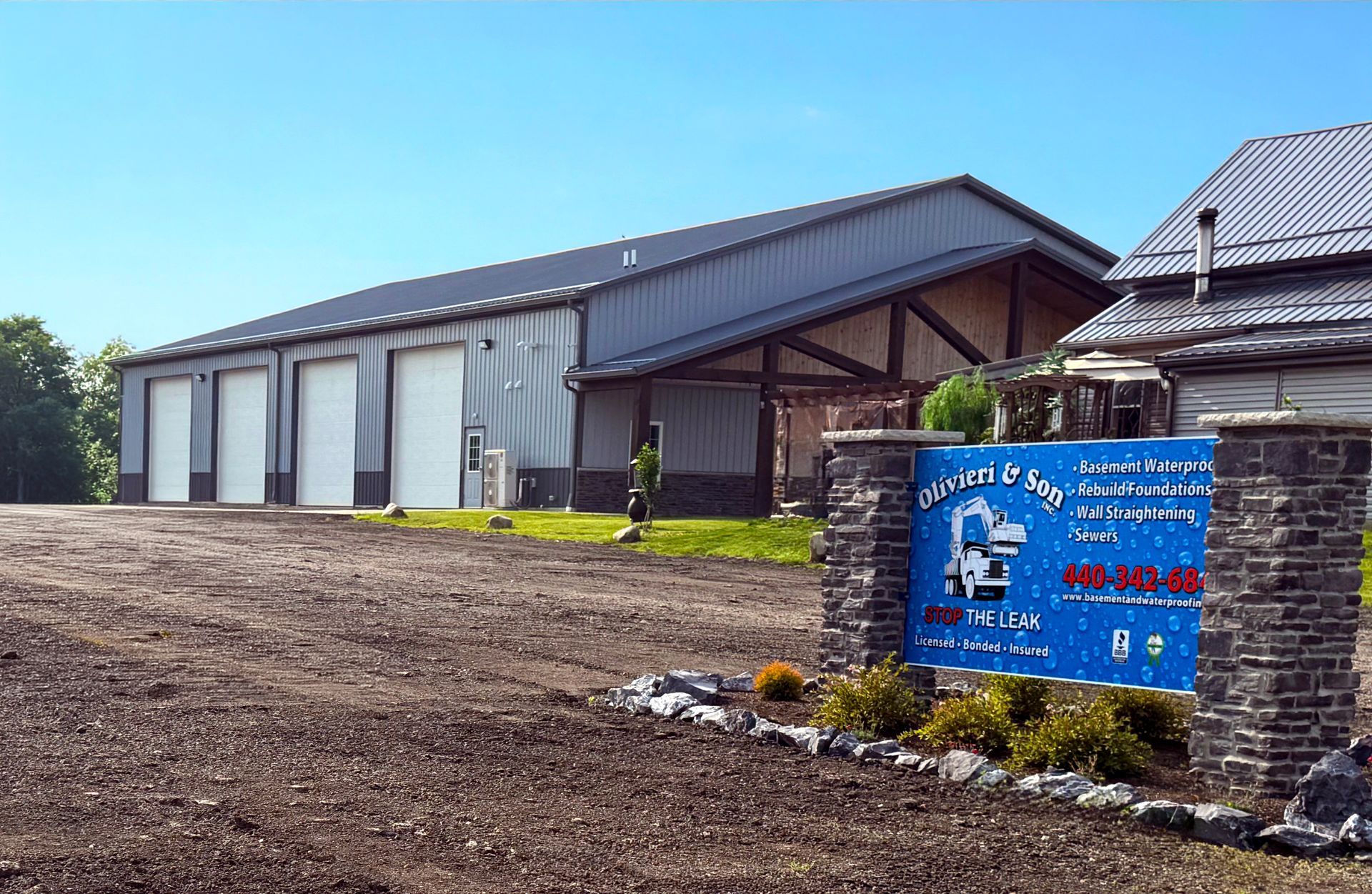 A gray commercial building with four garage bays sits behind a blue business sign on a stone monument.