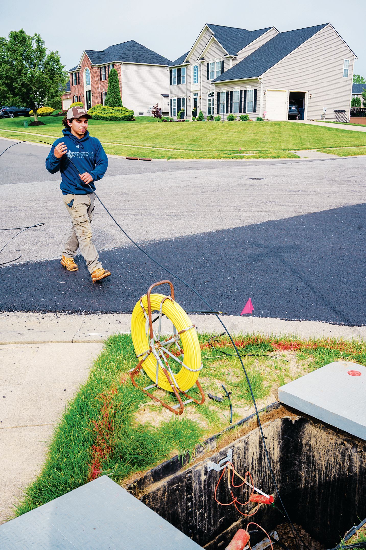 A technician uses a yellow cable reel to inspect underground utility lines near an open access hatch in a suburban street.