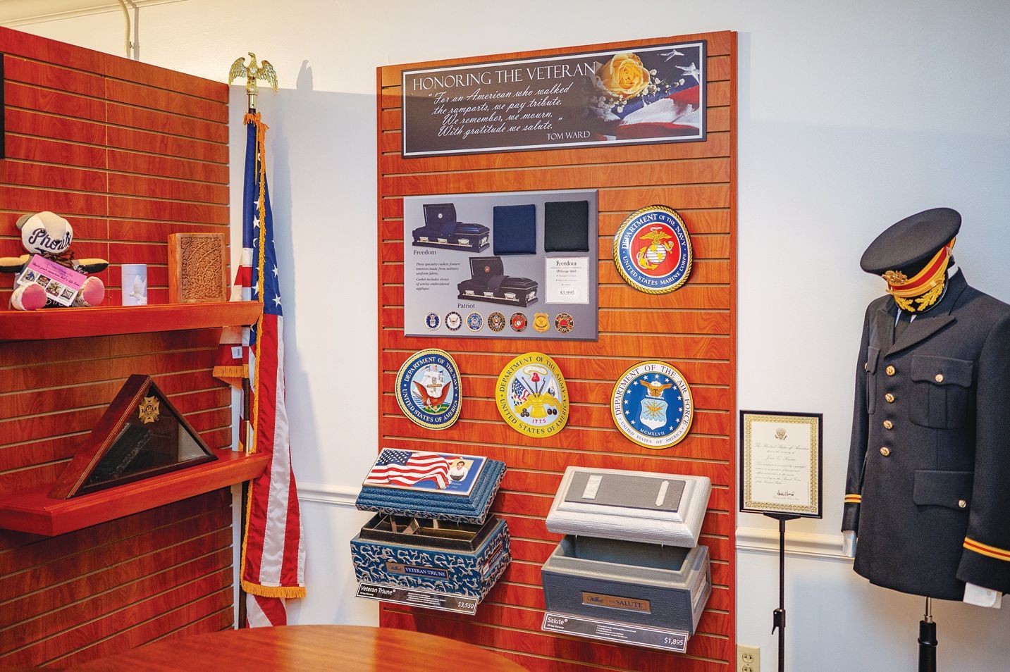 A display of military memorabilia, including uniform emblems, service branch plaques, a flag, and a formal dress coat.