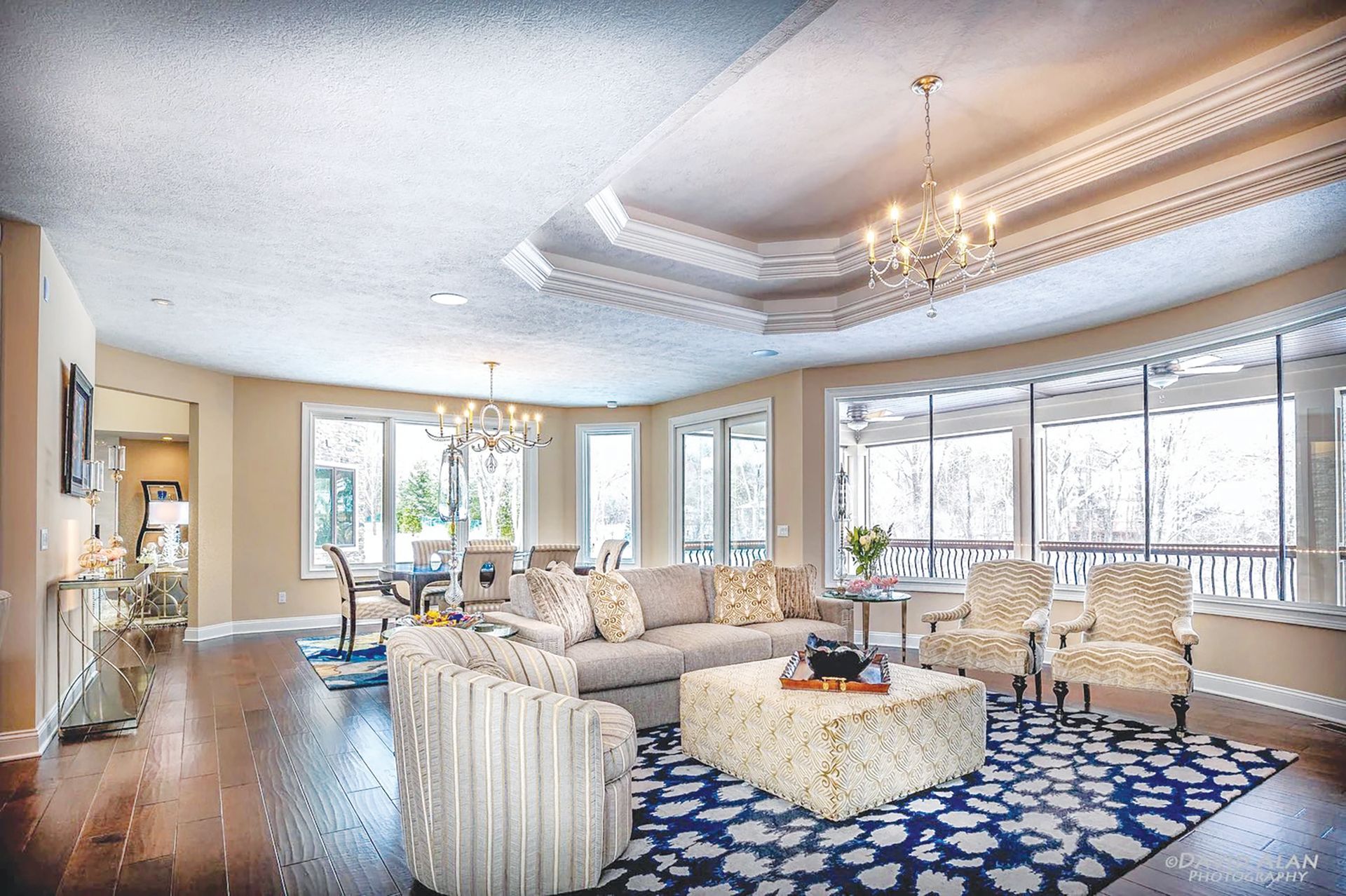 A living room with a large gray sofa, two patterned armchairs, a white square coffee table, and a blue and white area rug.