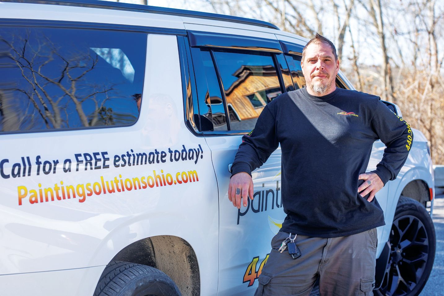 A person stands next to a white service vehicle displaying the website Paintingsolutionsohio.com and a free estimate offer.