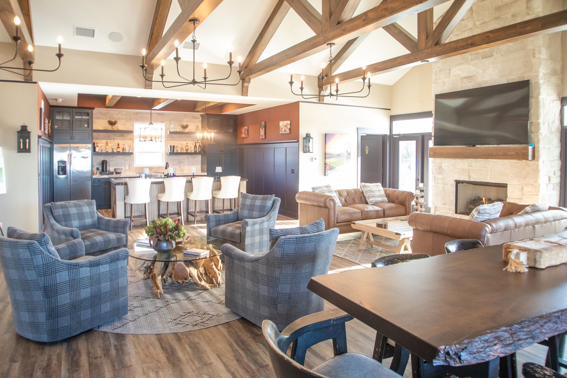 An open-concept living area with a stone fireplace, brown leather sofas, patterned armchairs, and a kitchen island bar.