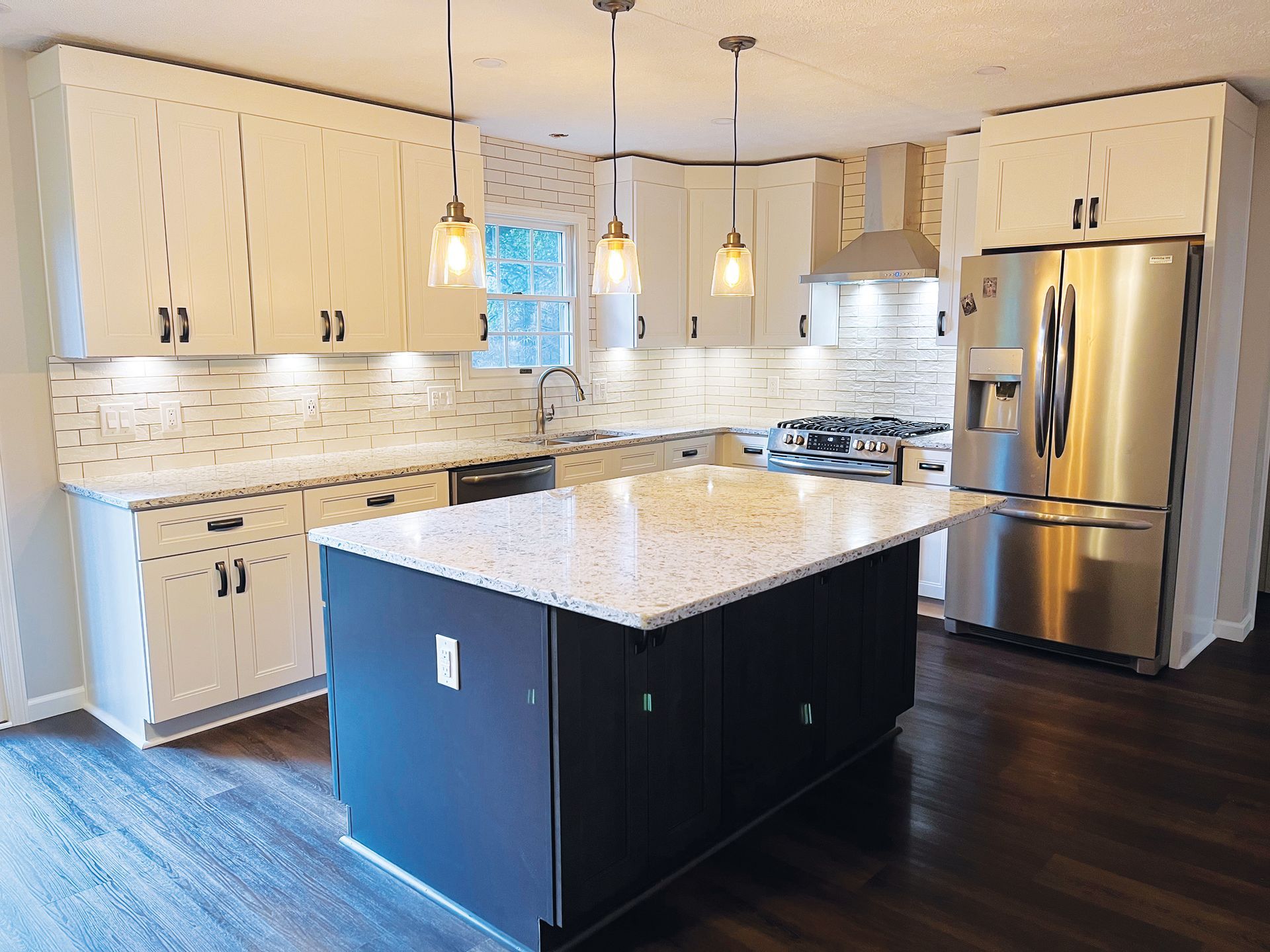 A modern kitchen with off-white cabinets, speckled granite countertops, a dark blue center island, and stainless appliances.