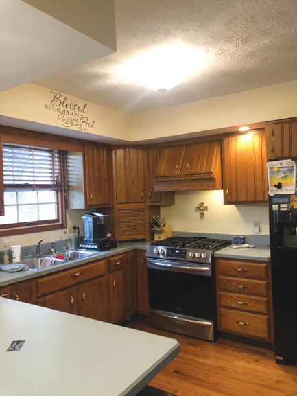 A kitchen with wooden cabinets, a stainless steel stove, a grey countertop, and a window with blinds.