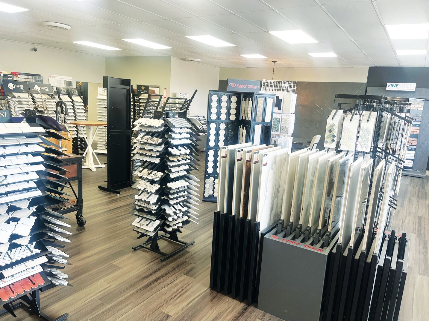 A retail store interior featuring multiple floor racks filled with rows of fabric or wallpaper sample swatches.