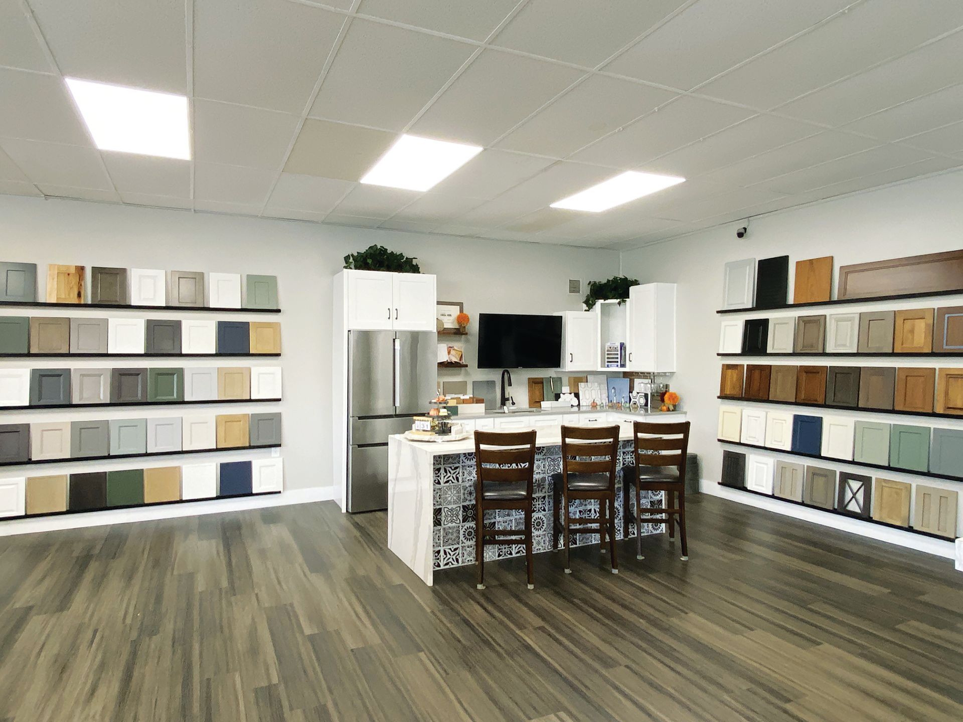 A kitchen design showroom featuring walls of sample cabinet doors, a central island with stools, and a refrigerator.