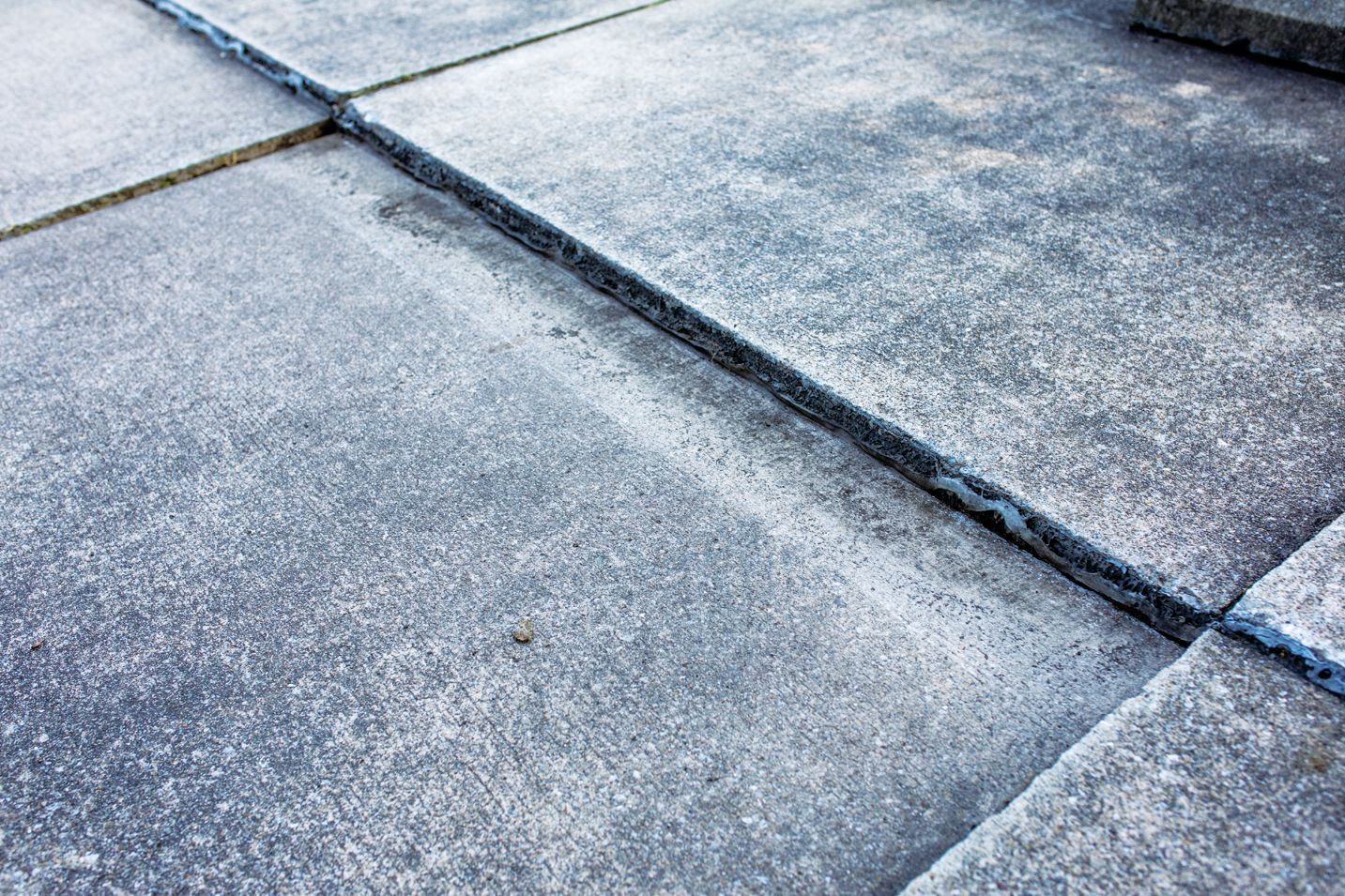 A close-up view of grey, square concrete paving stones with visible gaps between them.