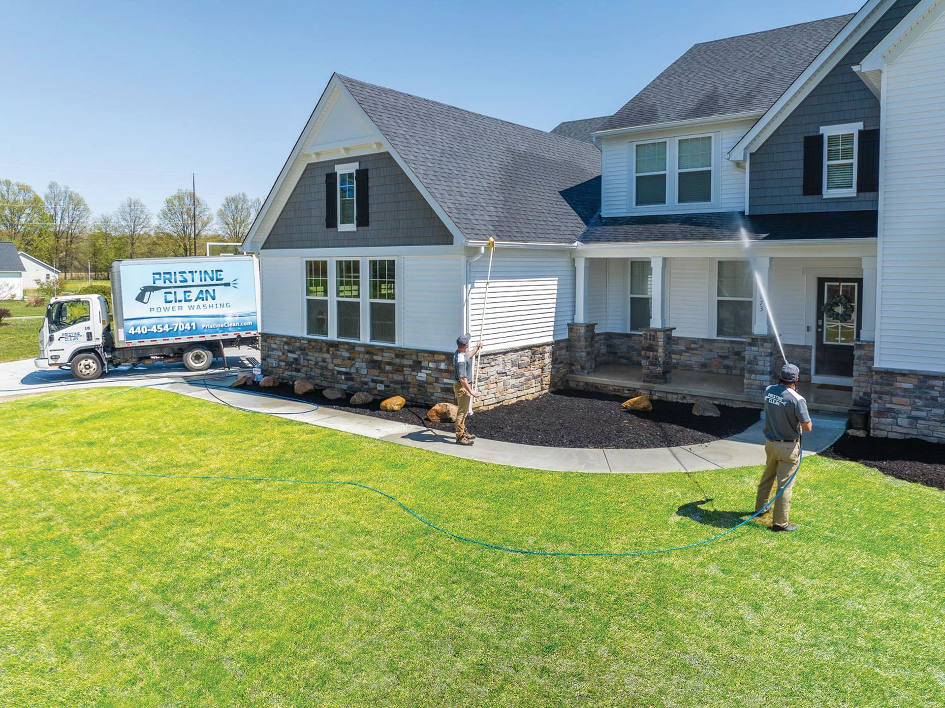 A technician pressure washes the siding of a suburban home near a company truck parked on the lawn.