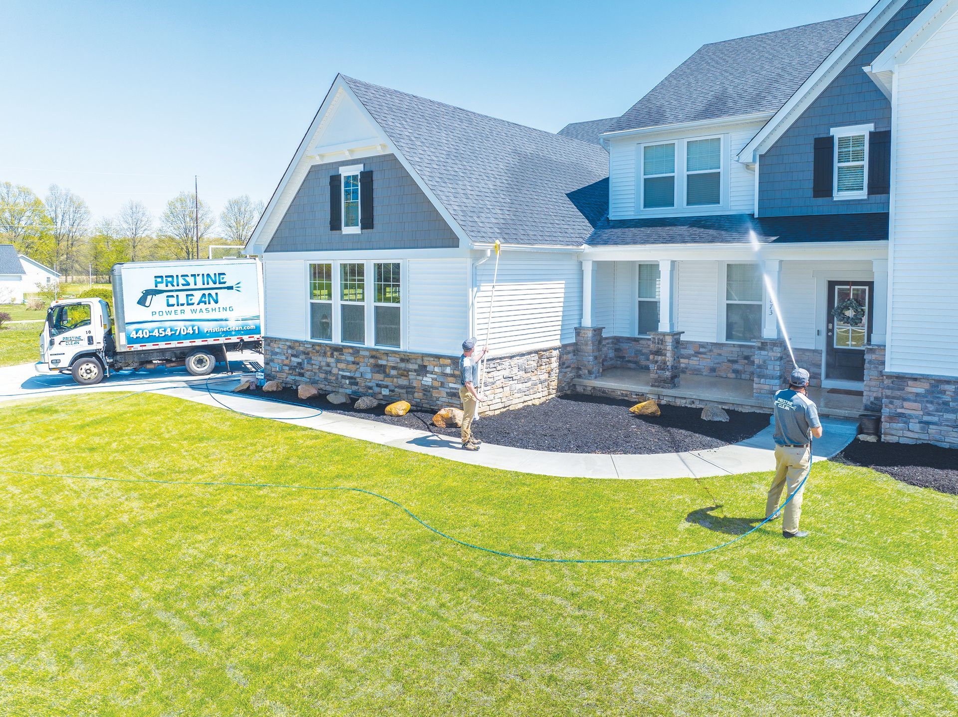 A service technician uses a high-pressure spray wand to clean the exterior of a white, two-story suburban house.
