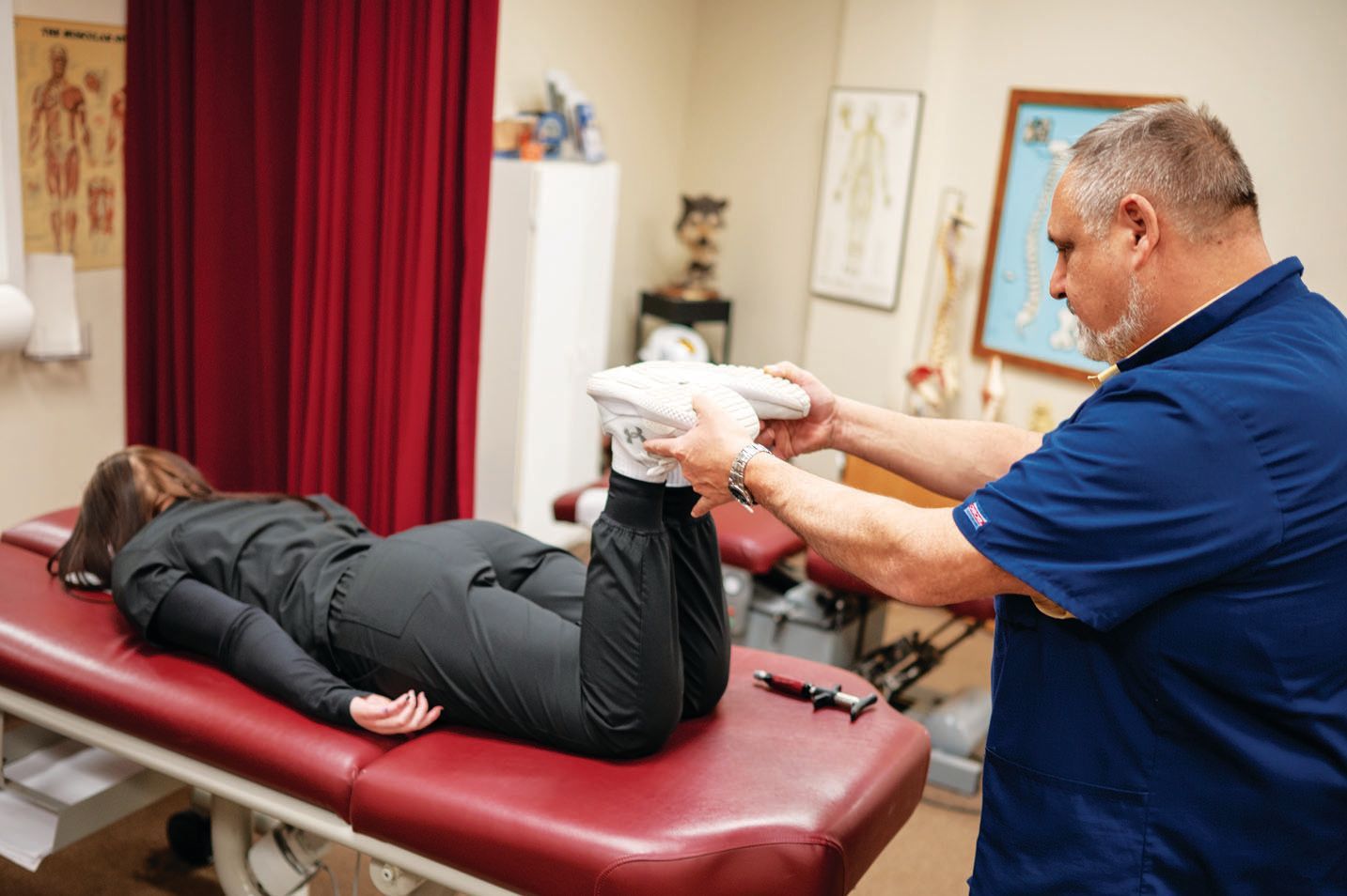 A practitioner in a blue shirt performs a physical examination on a person lying face down on a clinical table.