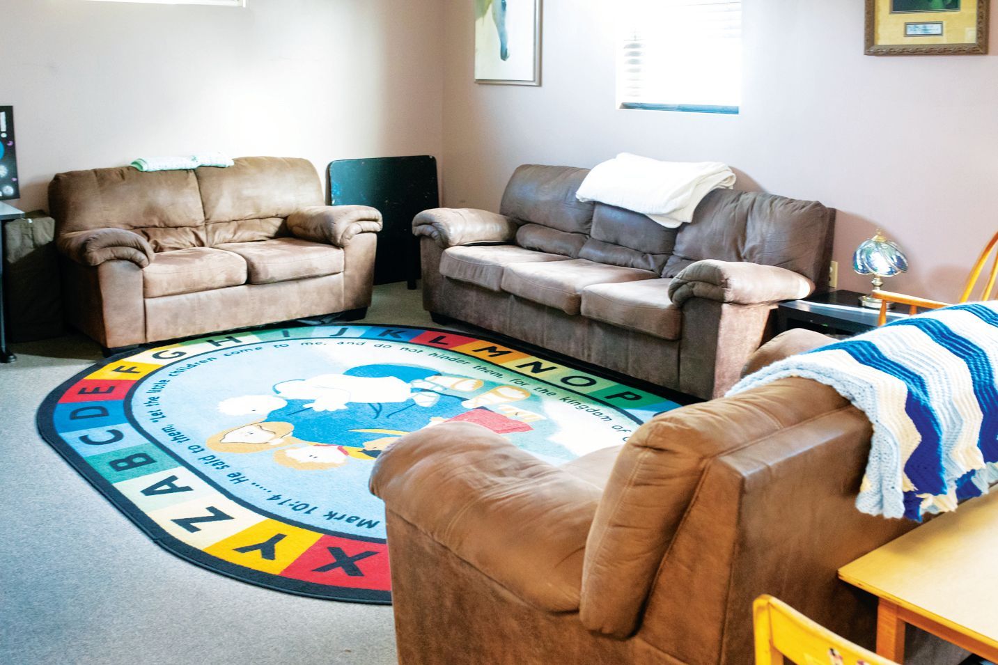 A cozy room with three brown couches arranged around a colorful circular rug featuring the alphabet and a map.