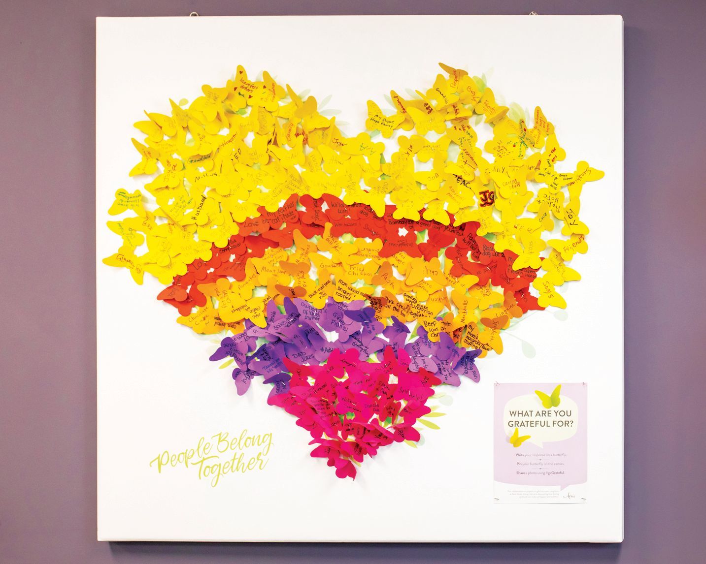 A heart-shaped collage of paper butterflies in yellow, orange, purple, and pink, with text and a small note on a white board.