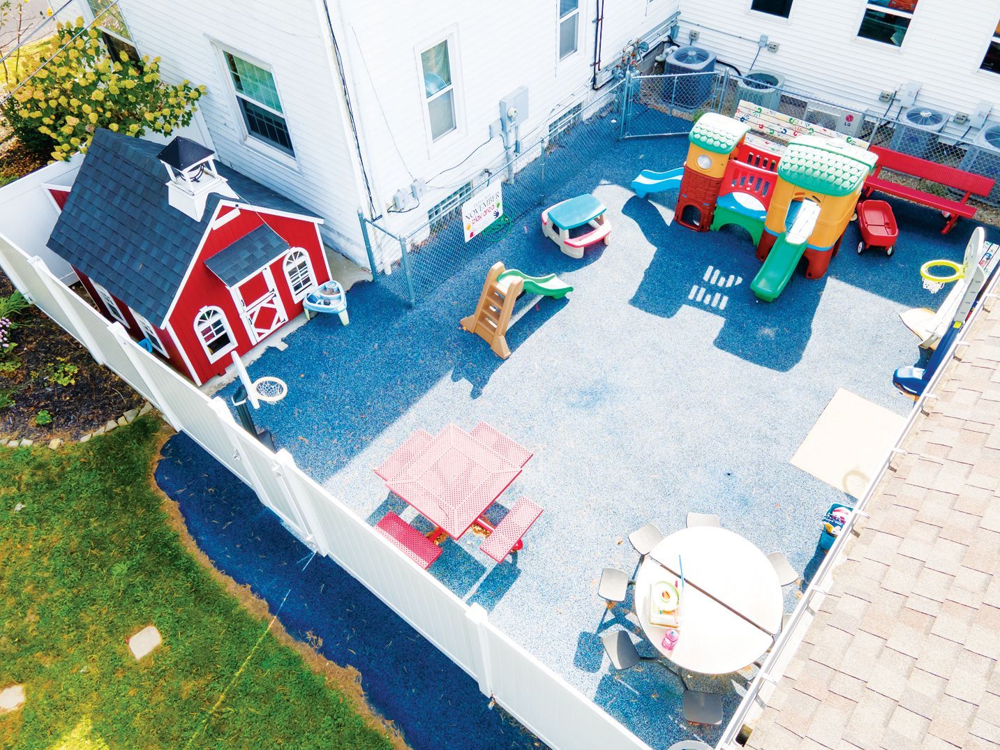 High-angle shot of a backyard daycare area with a red playhouse, a colorful slide structure, and outdoor seating.