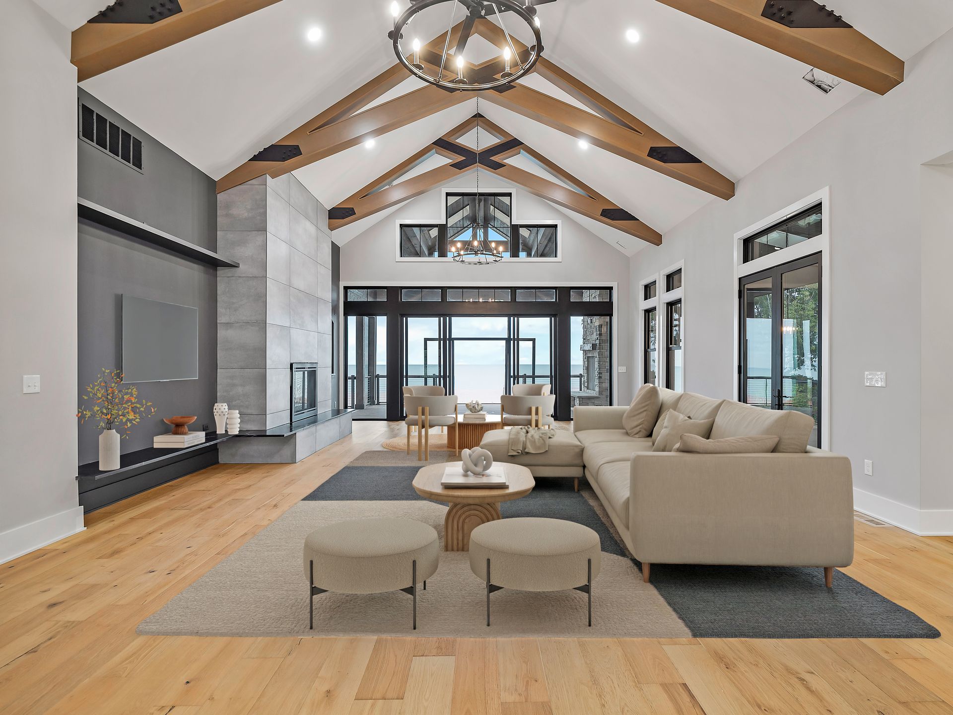 A spacious, modern living room with a vaulted ceiling, exposed wooden beams, a stone fireplace, and beige furniture.