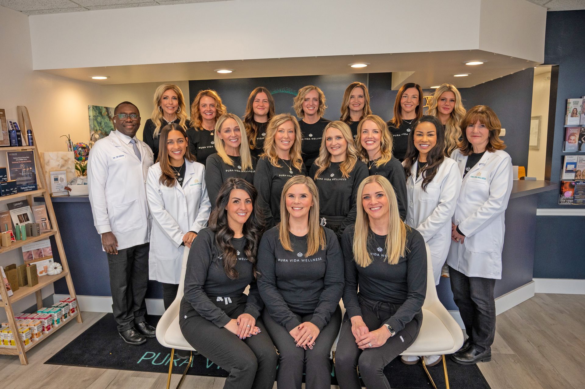 A large group of staff members in professional attire and scrubs stand together in a bright, modern medical office.
