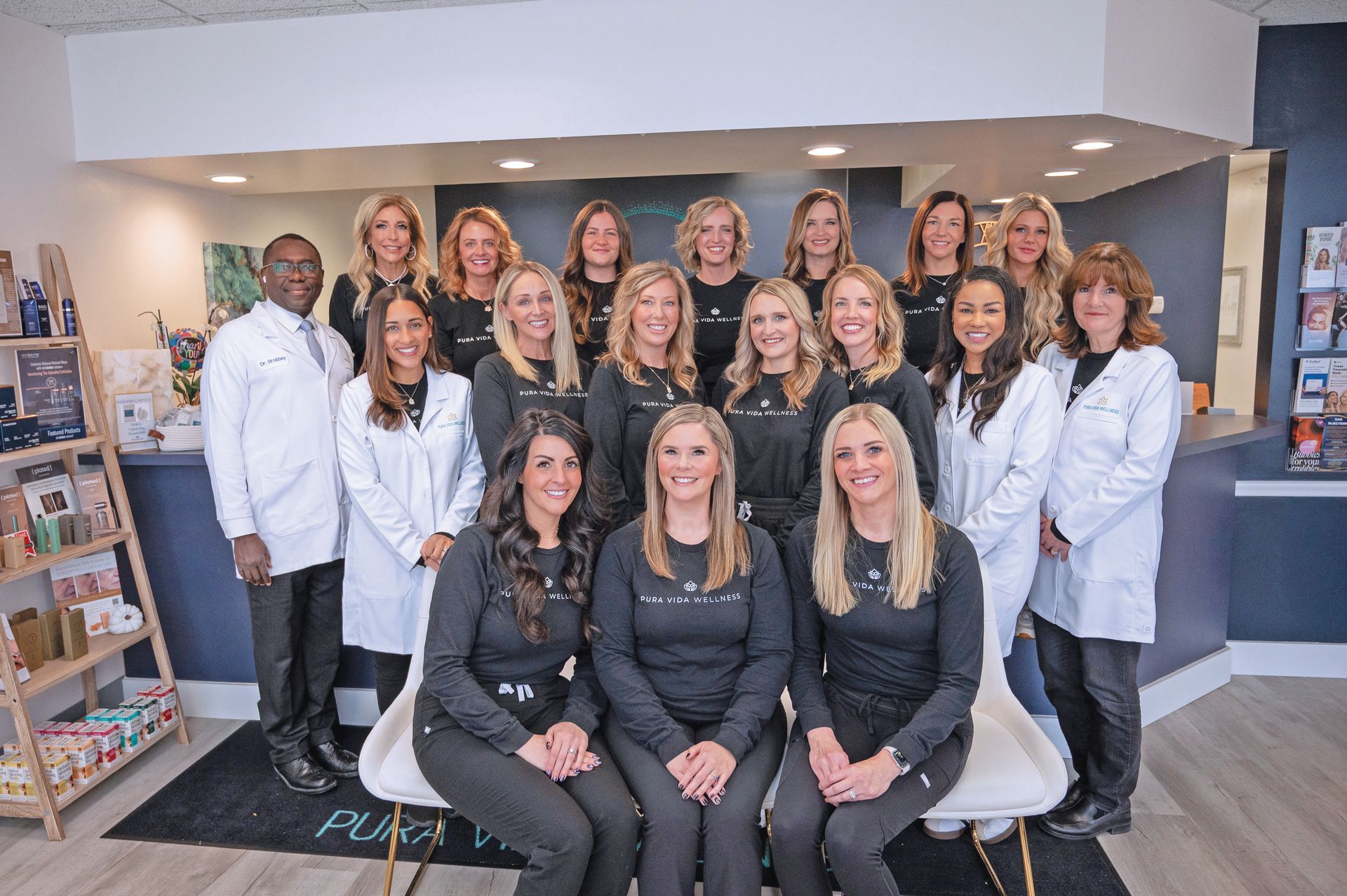 A diverse group of staff members in professional attire pose together inside an office clinic setting.