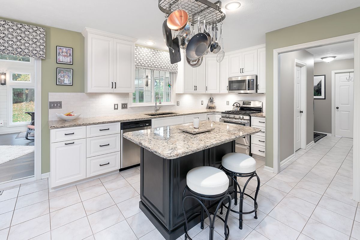 Modern kitchen with white cabinets, a dark island with two stools, granite countertops, and a hanging pot rack.