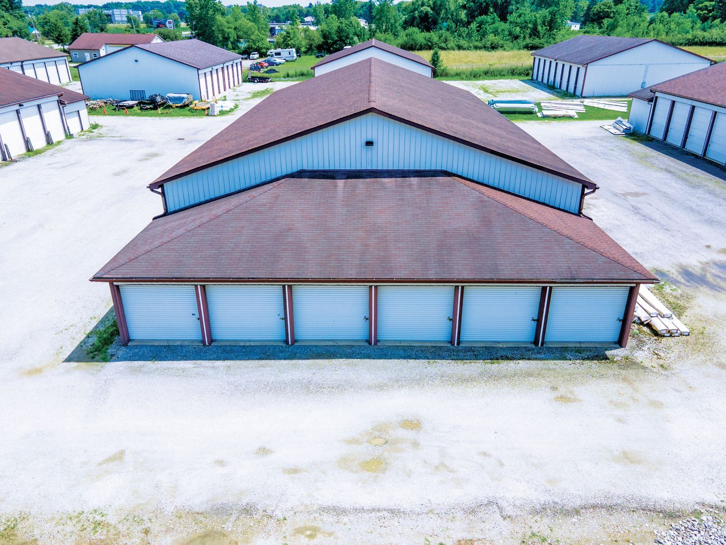 An aerial view of a self-storage facility featuring multiple grey buildings with brown roofs on a gravel lot.