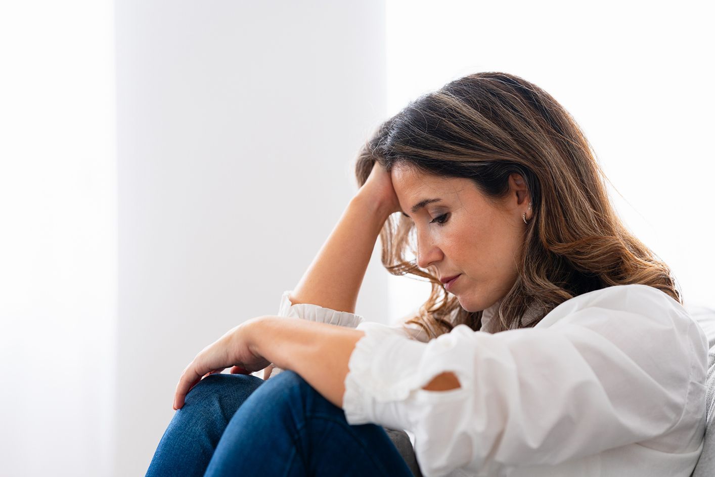 A person with dark hair sits with their head resting on their hand, appearing thoughtful or distressed.
