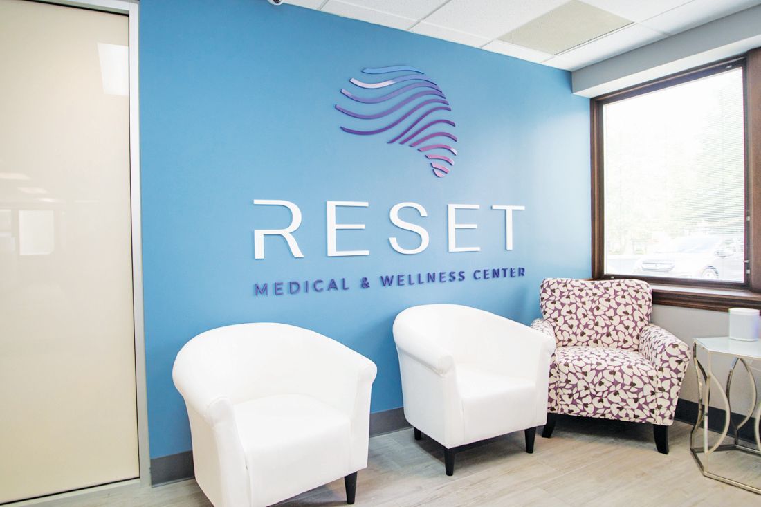 Waiting area of Reset Medical & Wellness Center with blue walls, white signage, and three chairs near a window.