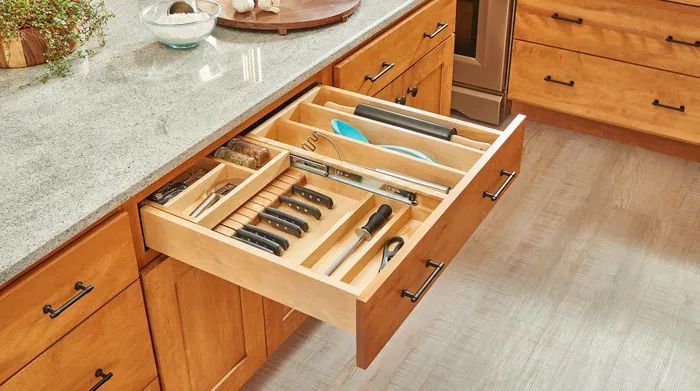 An open wooden kitchen drawer featuring a built-in organizer filled with various kitchen utensils and tools.