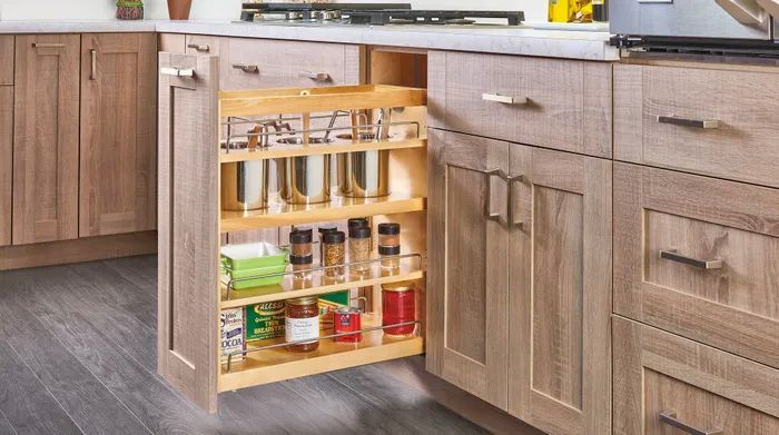 A narrow wooden kitchen cabinet pull-out organizer filled with spices and condiments, integrated into a modern kitchen.