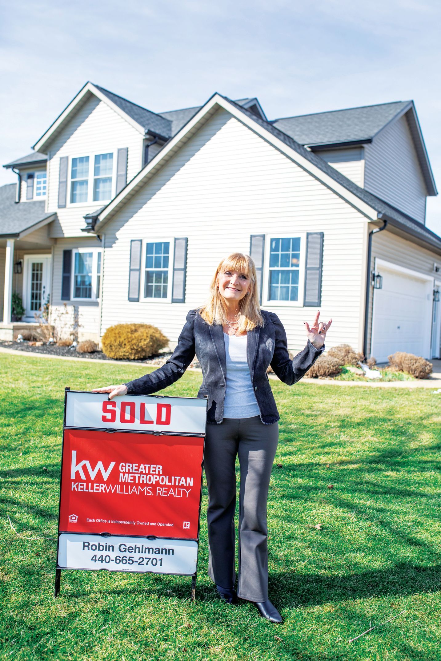 A person stands smiling in front of a house next to a red 
