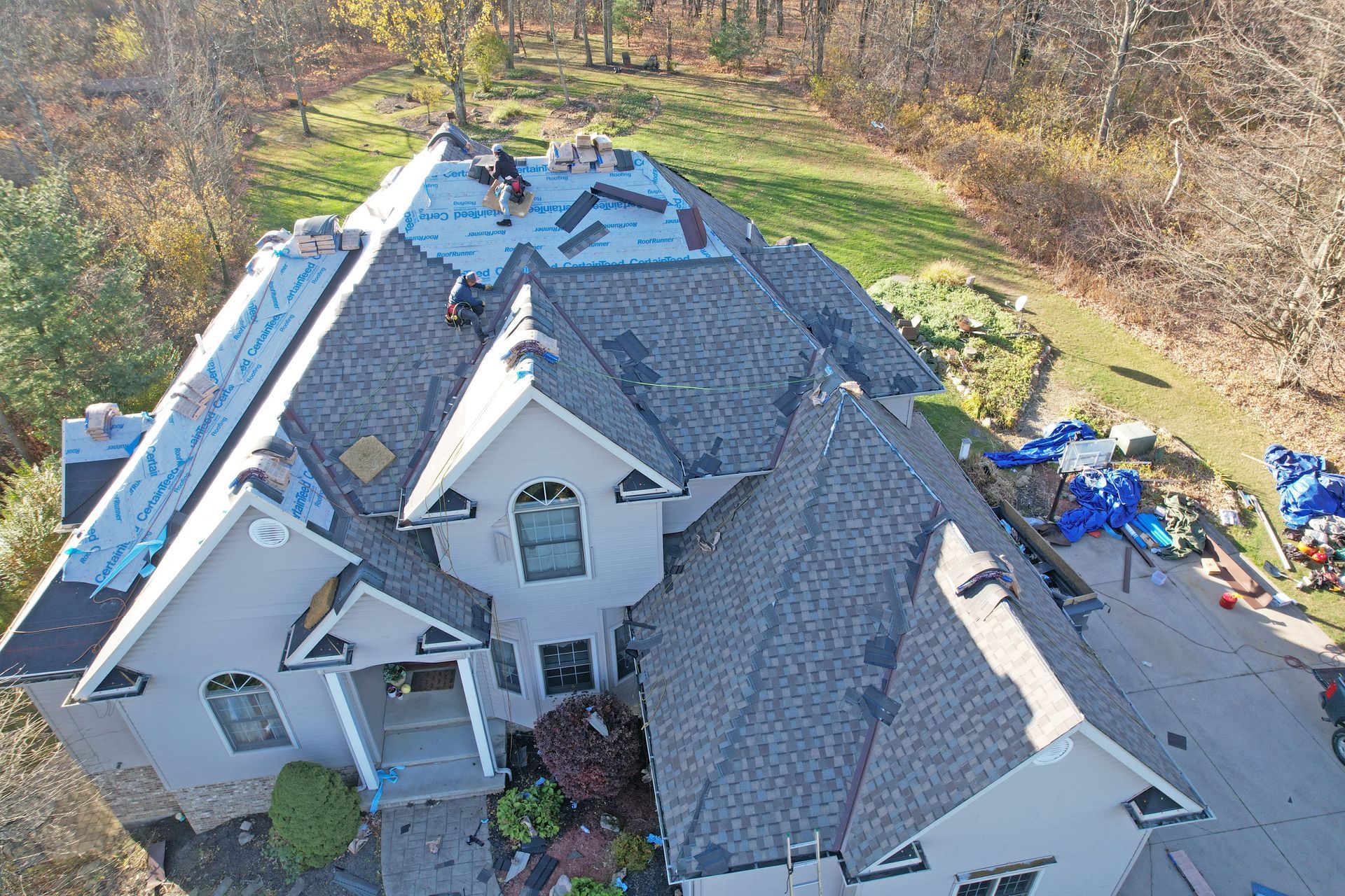 Aerial view of a residential roof replacement in progress, with workers installing new gray shingles.