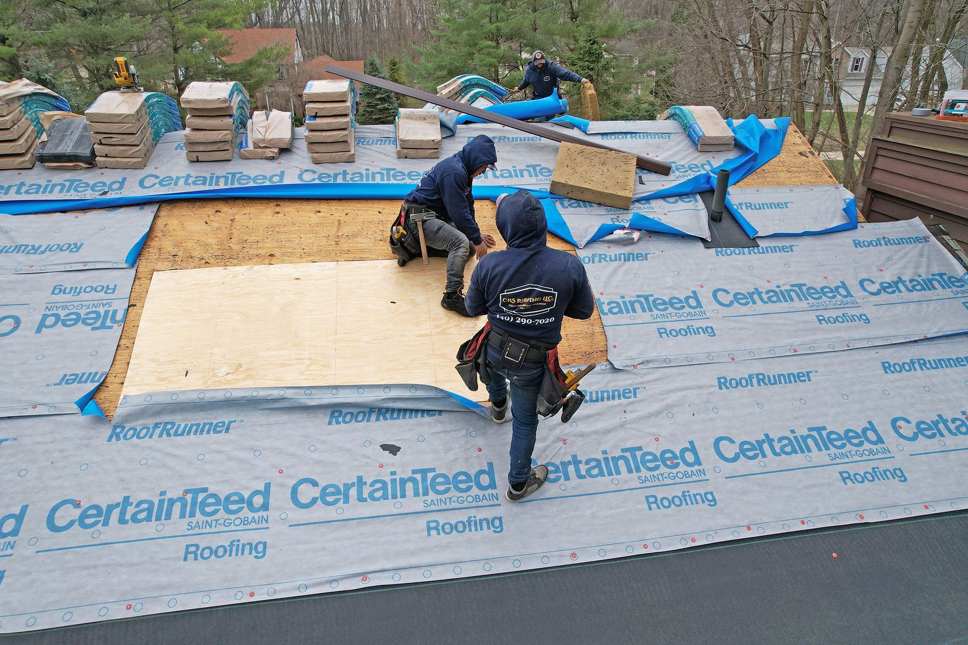 Construction workers installing new plywood roof decking over gray underlayment on a residential roof.