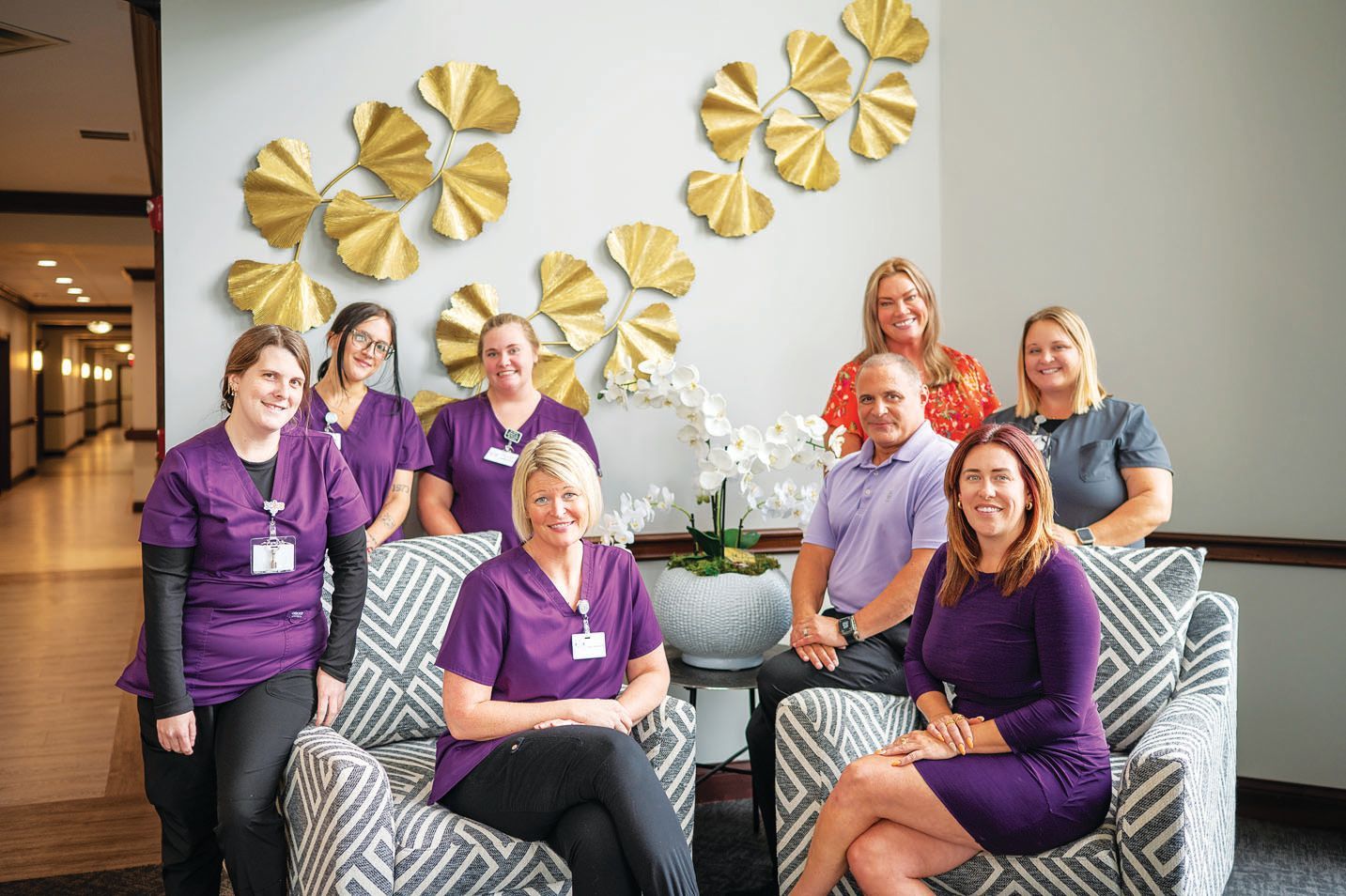 A group of eight staff members, mostly in purple uniforms, pose for a portrait in a modern, professional lobby.