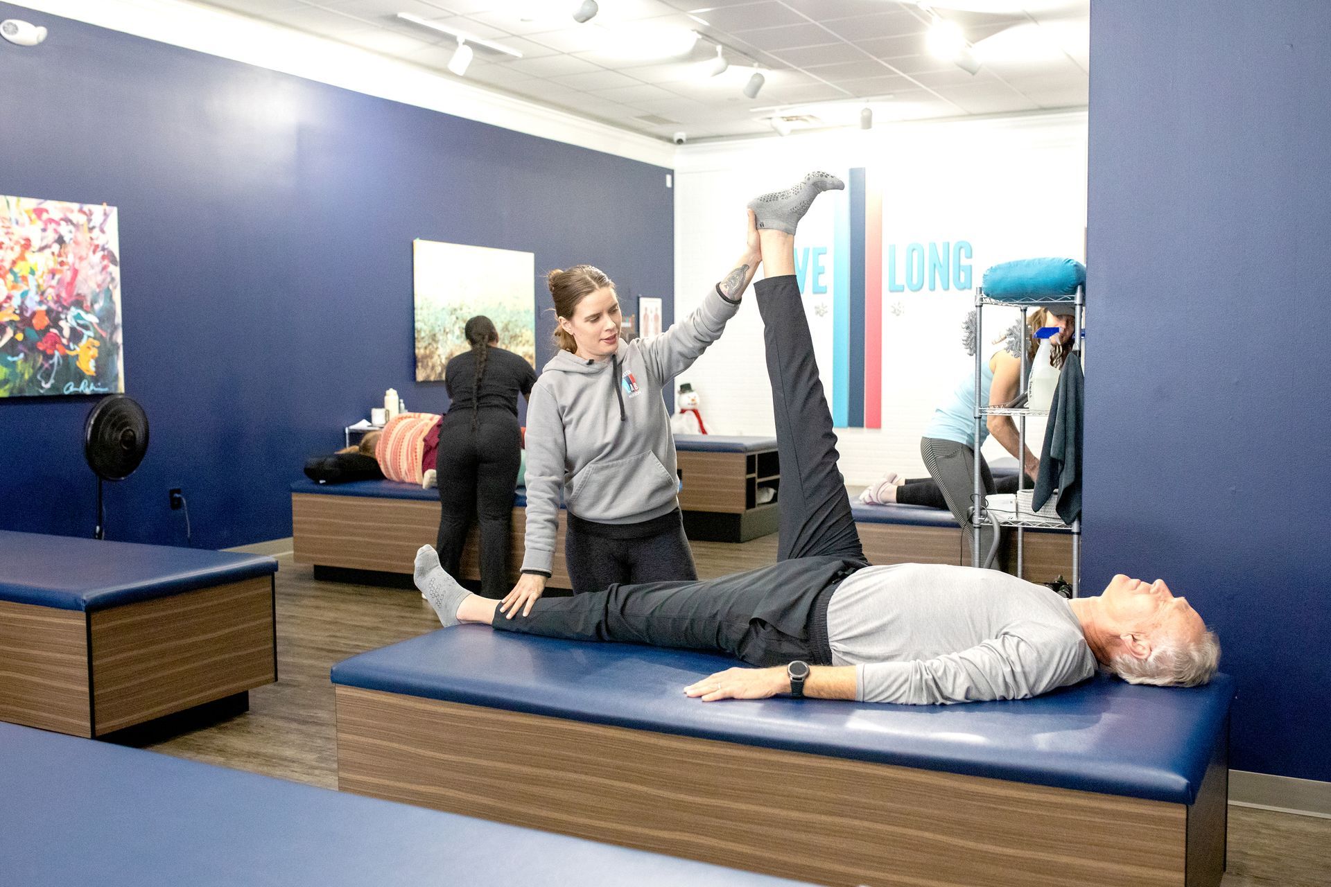 A practitioner stretches a client’s leg while they lie on a blue massage table in a professional therapy room.