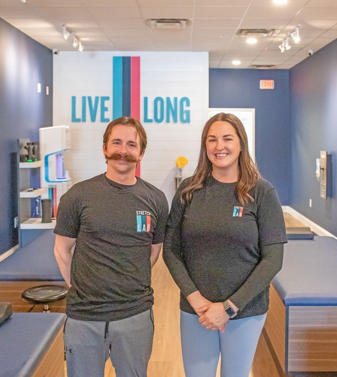 A man and a woman in matching grey shirts stand in a wellness center with a 