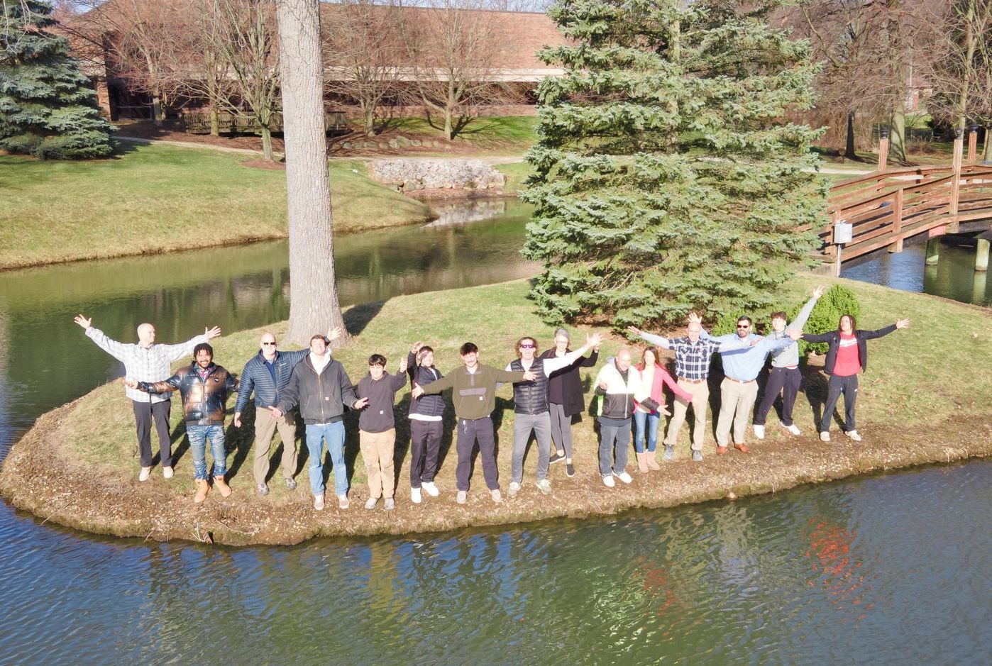 A group of people standing on a small grassy island in a pond, waving their arms with their hands raised.