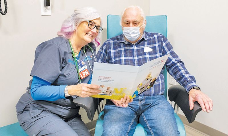 A nurse and a patient sitting in a clinical setting look together at a pamphlet held between them.
