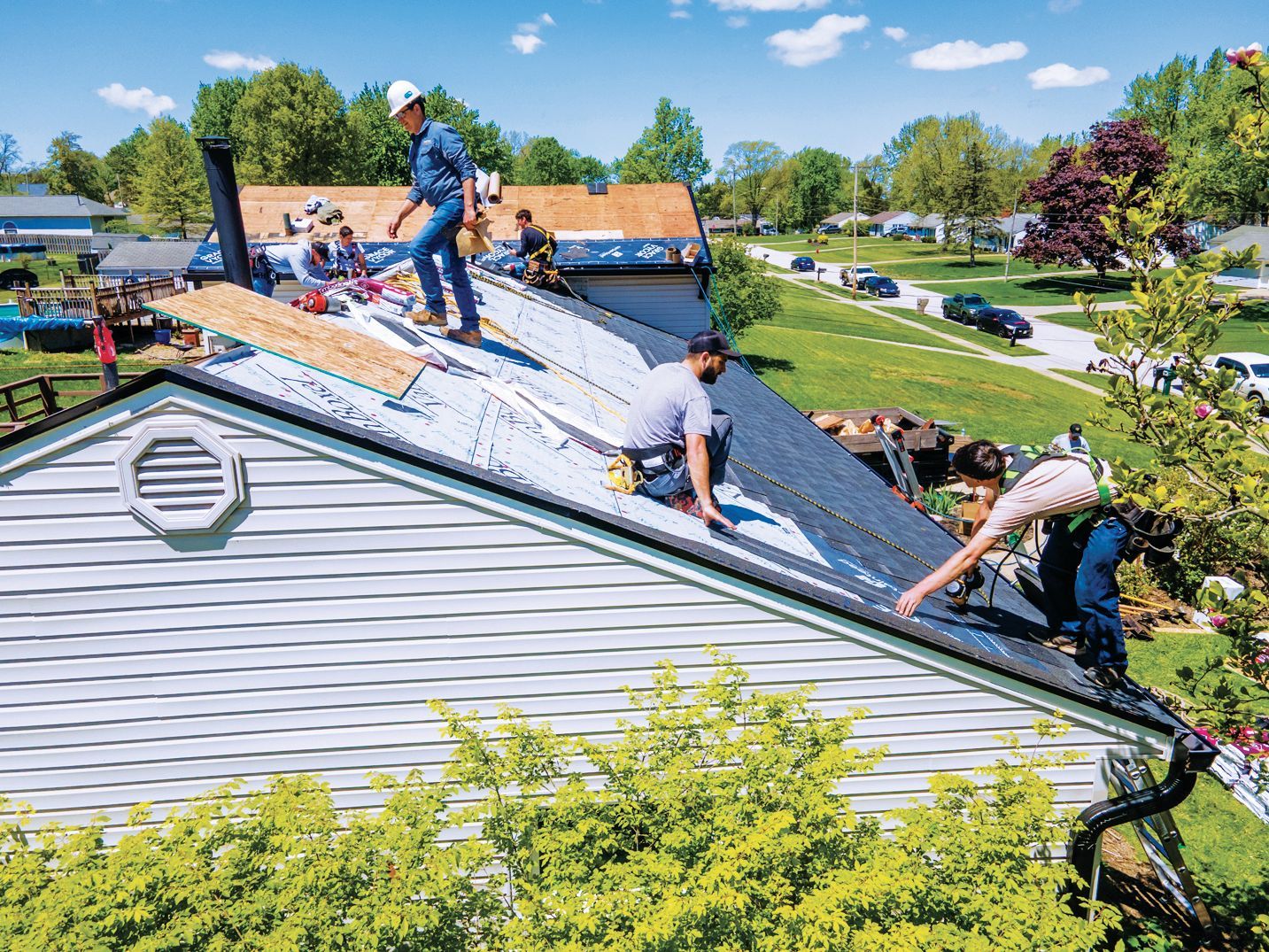 Construction workers in safety gear repair a residential roof on a sunny day.