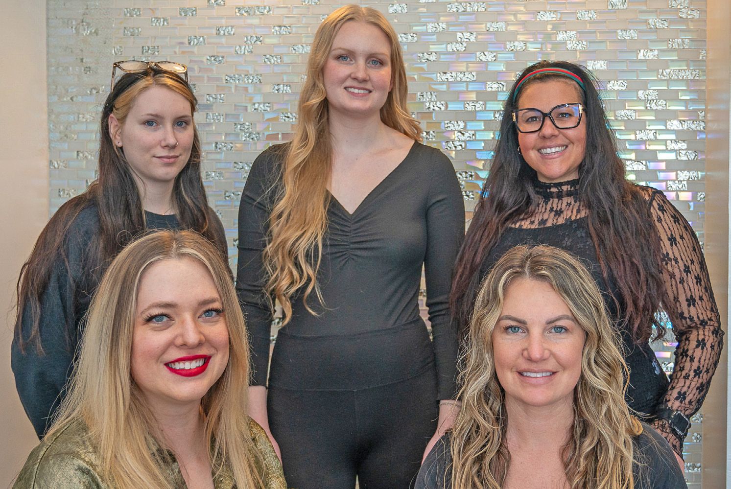 Five people smile and pose together in front of a decorative wall featuring light-colored, metallic eye-shaped icons.