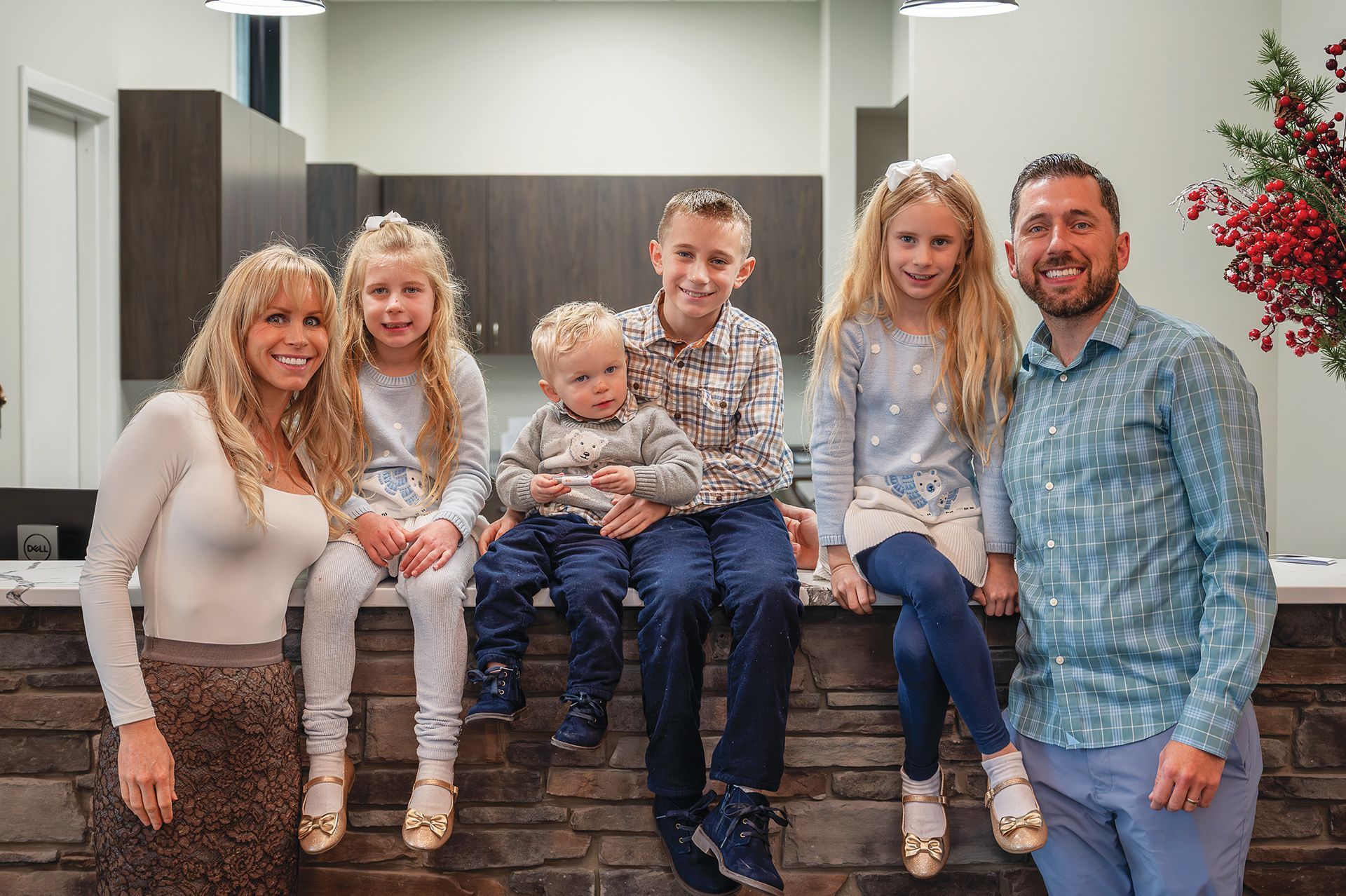 A family of six smiling while gathered indoors near a stone-faced counter with dark cabinets in the background.