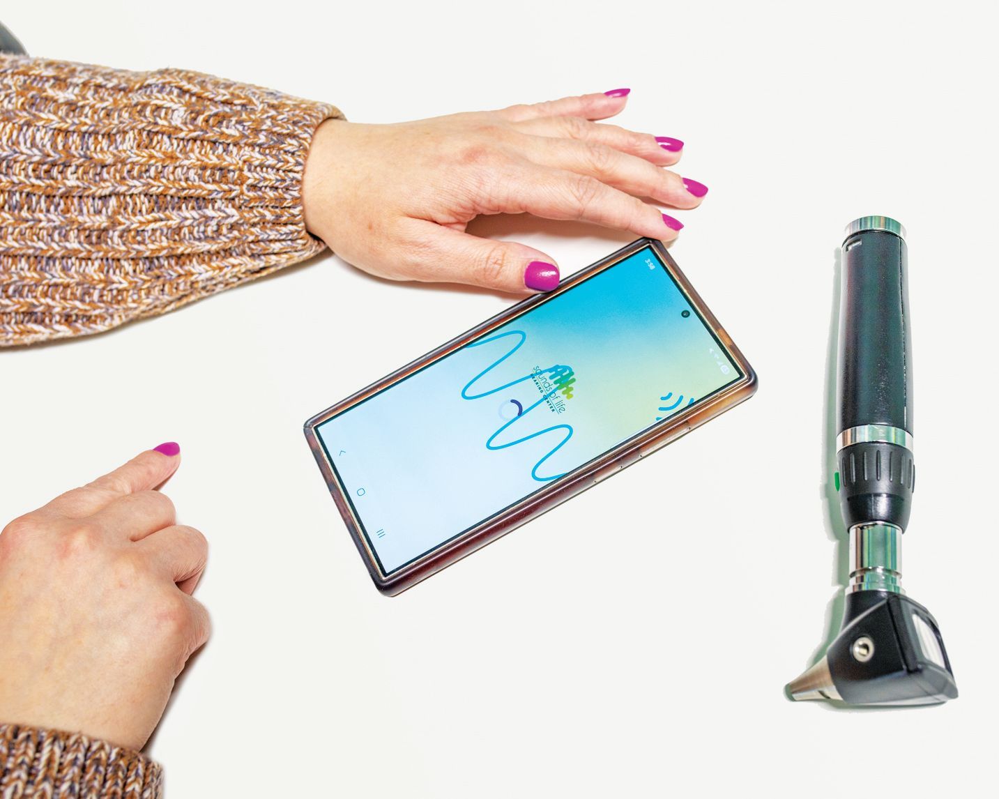 A person's hands rest near a smartphone displaying a wave icon and an otoscope on a white surface.