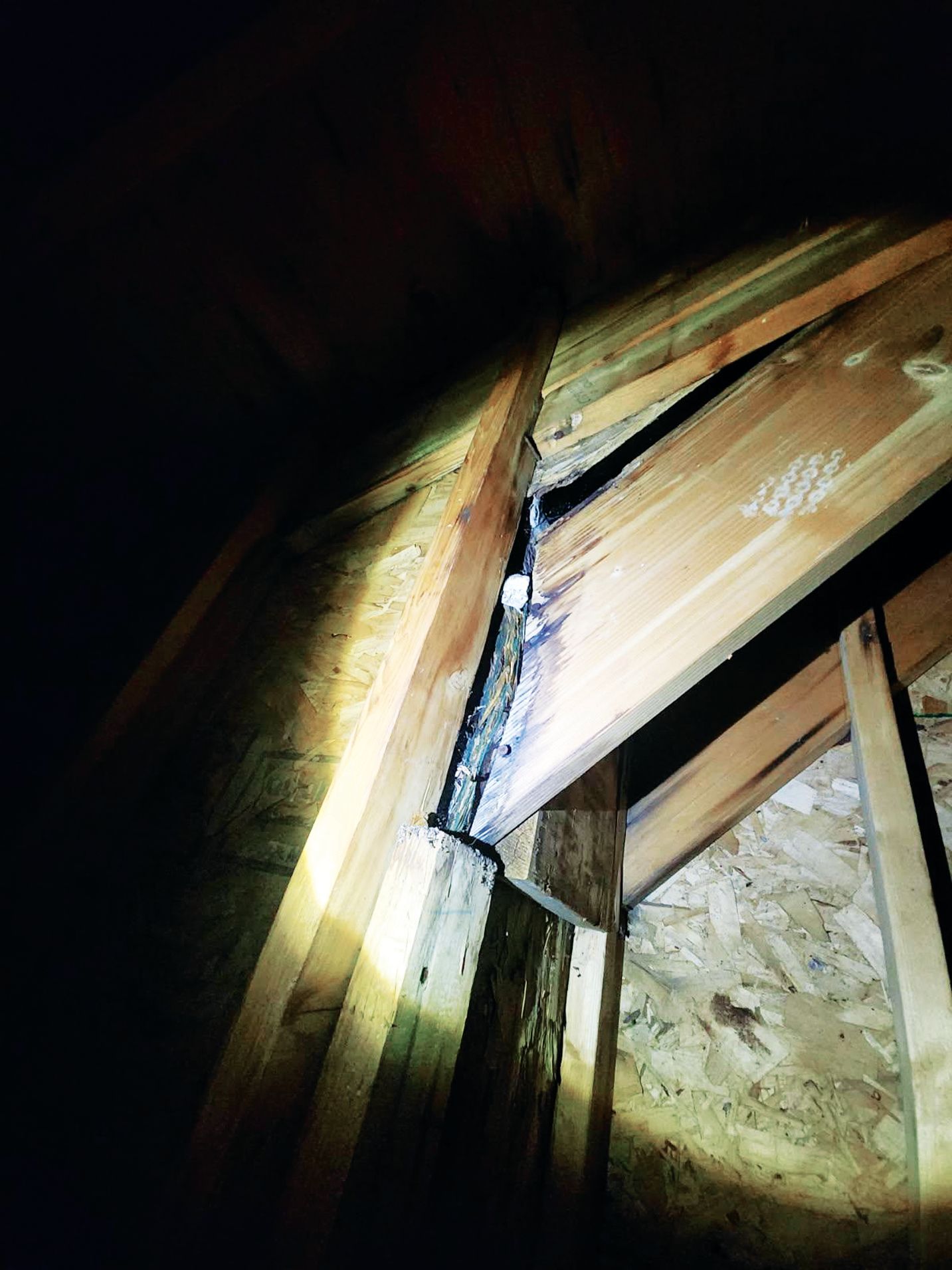 A close-up view of an attic structure showing a gap between a wooden joist and roof decking, with visible dark debris.