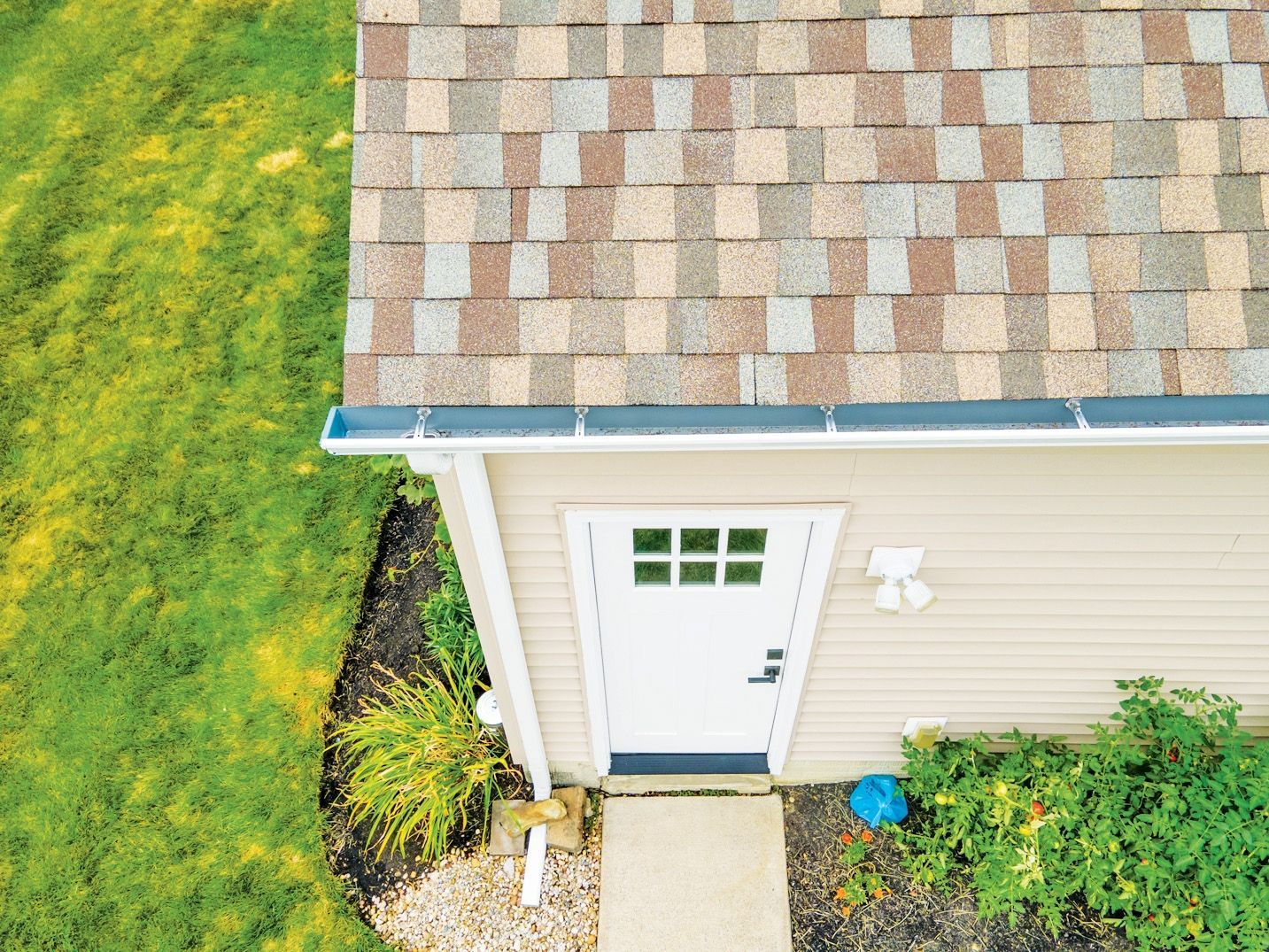 High-angle view of a house roof, white door, and green lawn, featuring asphalt shingles and a gray gutter system.