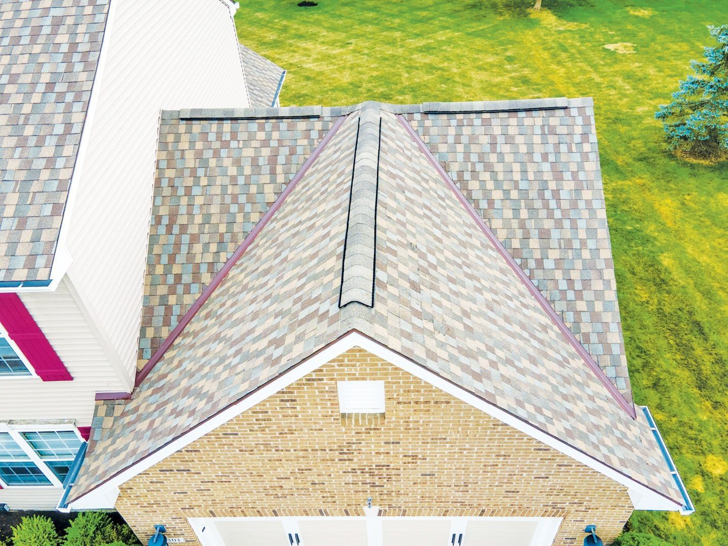 An aerial view of a tan brick house with a multi-gabled shingled roof and green lawn.