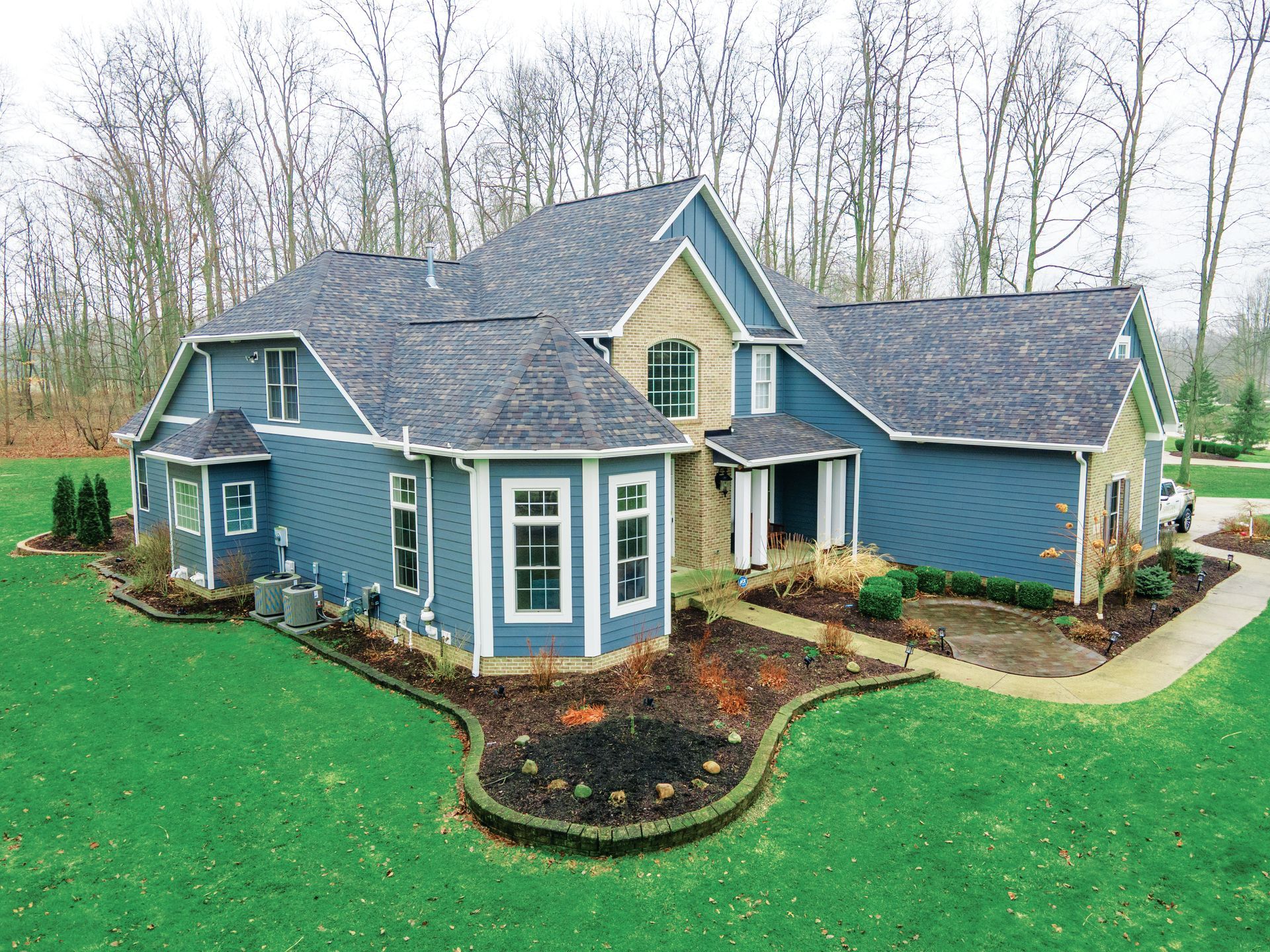 A blue multi-story home with a stone accent and dark shingled roof, set against a backdrop of trees and a green lawn.