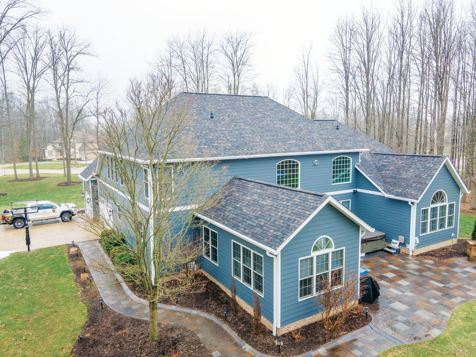 An aerial view of a multi-story, blue-sided house with a dark shingled roof, a stone patio, and a winding walkway.