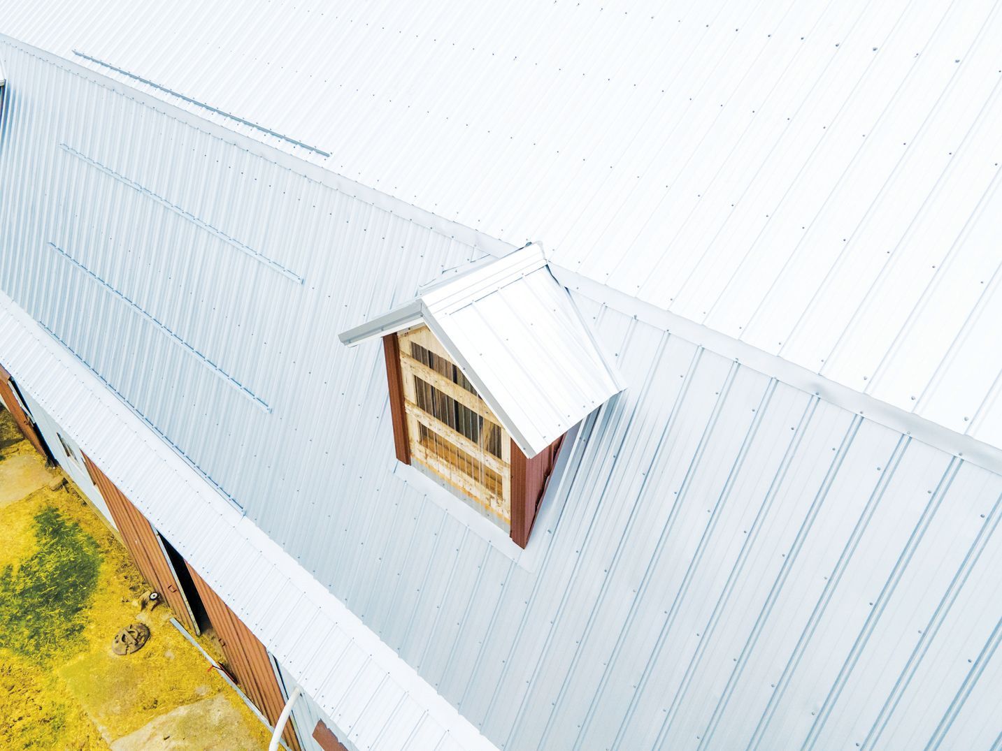 A small dormer window with a metal roof and wooden frame set into the corrugated metal roof of a barn.